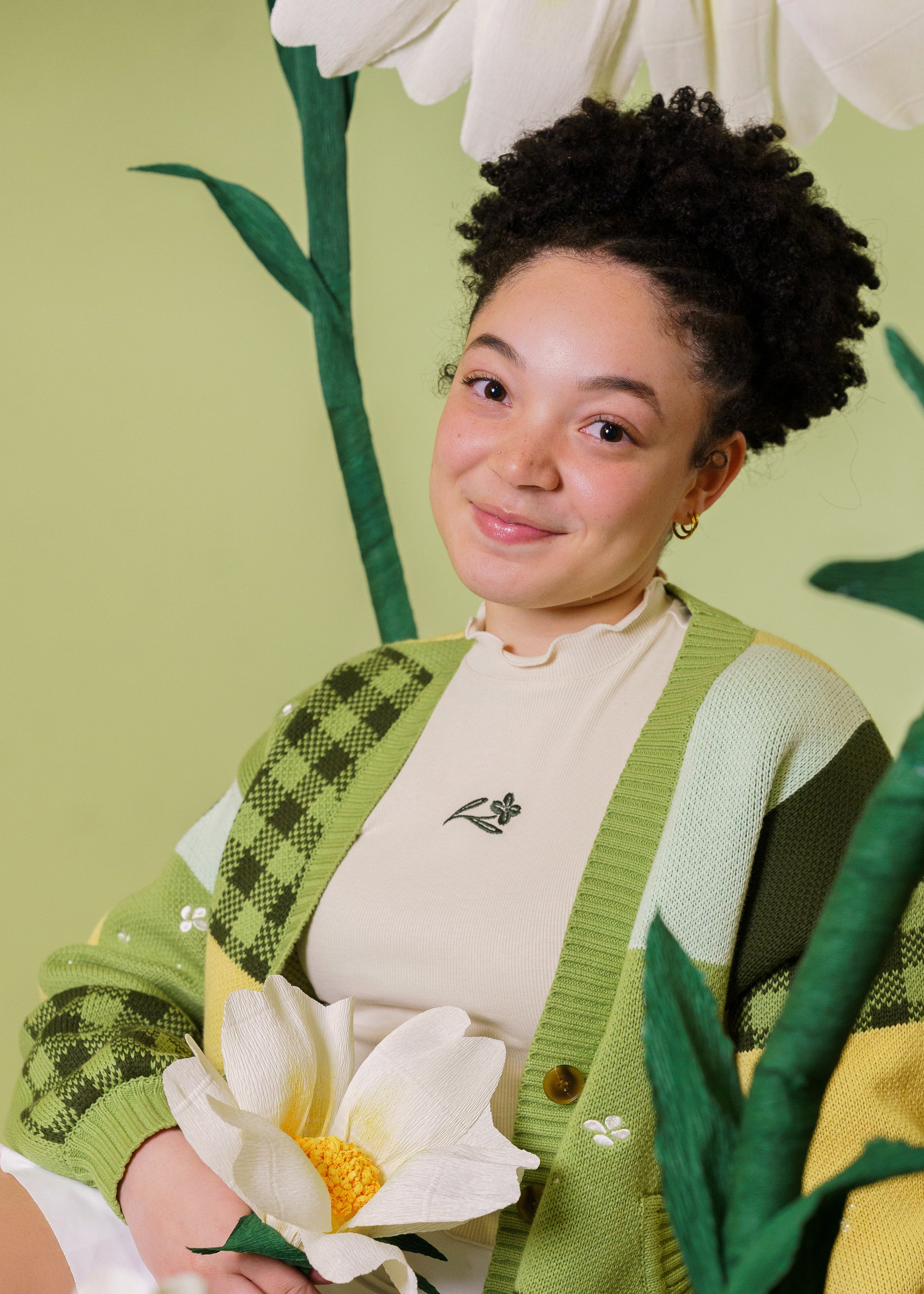 Person wearing a green cardigan with white flowers and a green background