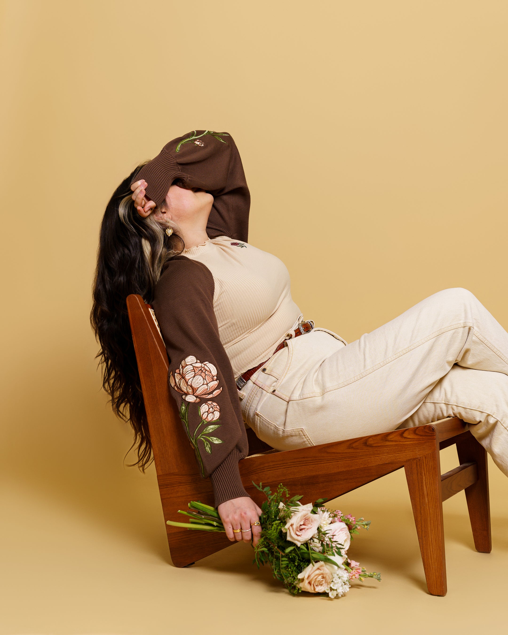 Woman wearing bashful brown bolero in size small sitting on chair holding a bouquet.