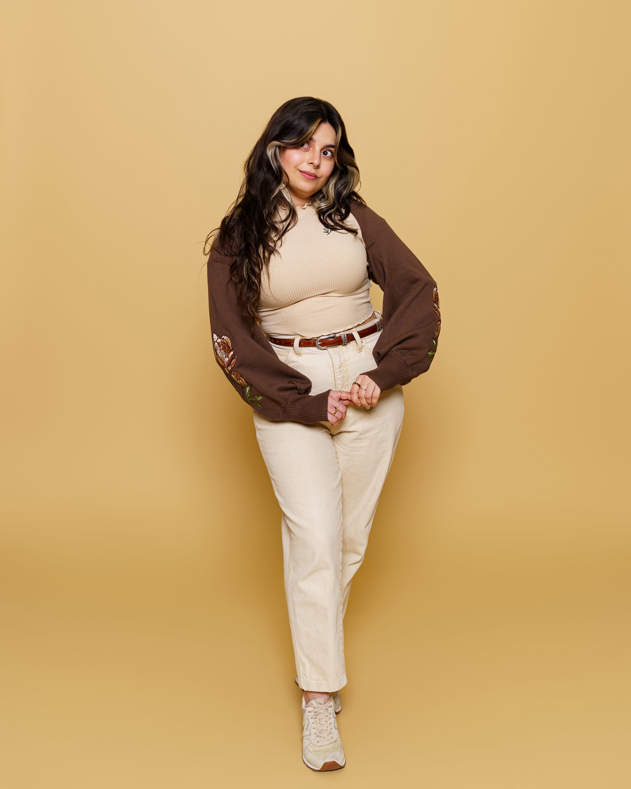 Woman wearing bashful bolero cardigan in size small with off-white pants in front of soft yellow background.