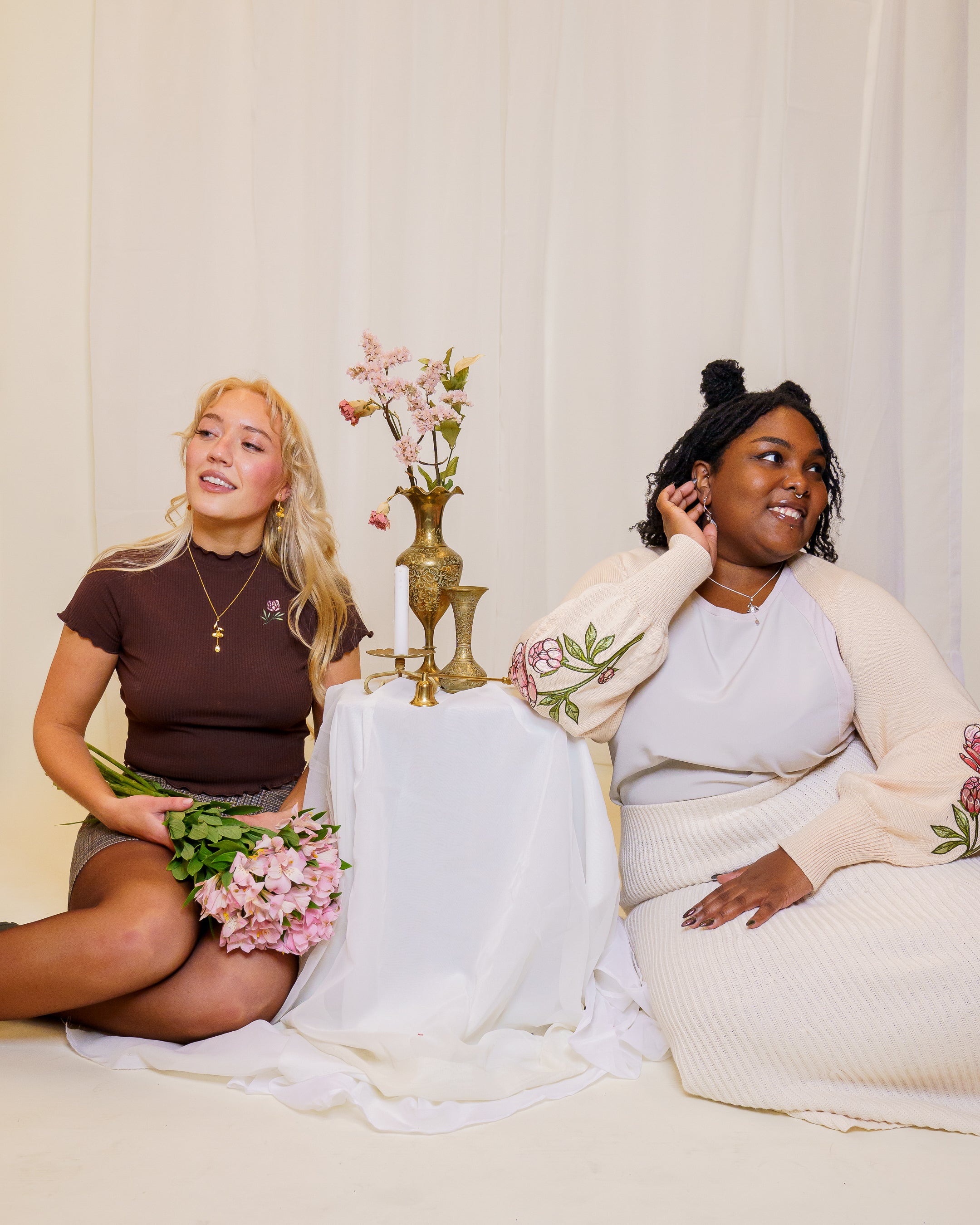 Two woman sitting with one wearing the bashful cream bolero and the other wearing the freshly picked brown mini tee.