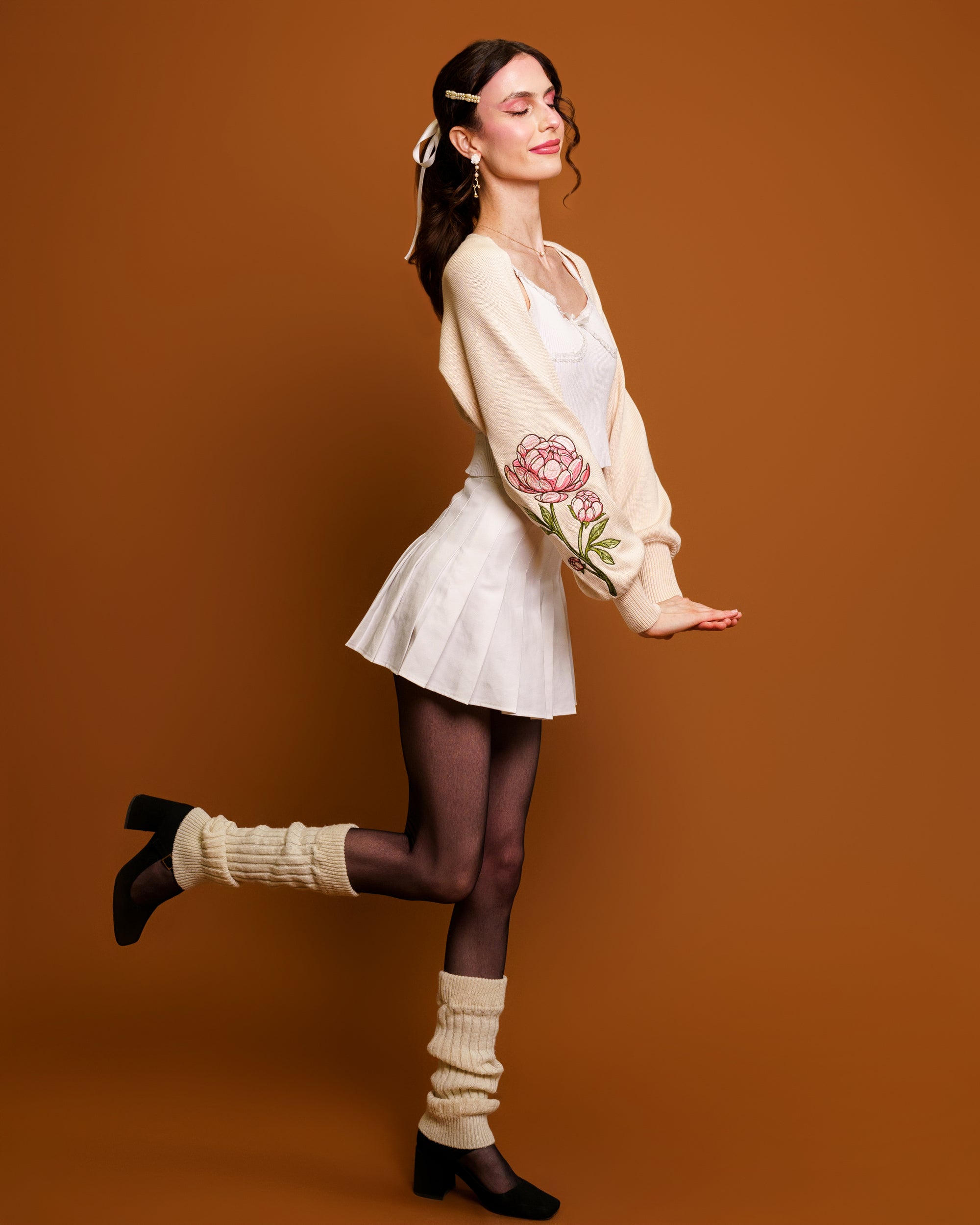 Woman wearing bashful cream bolero in size extra small posing in front of orange background.