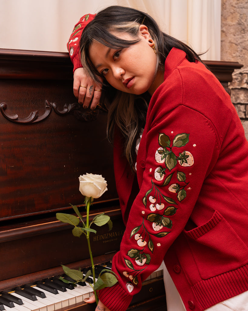 Model wearing berry blend cardigan in size large posing with a white rose and paino.