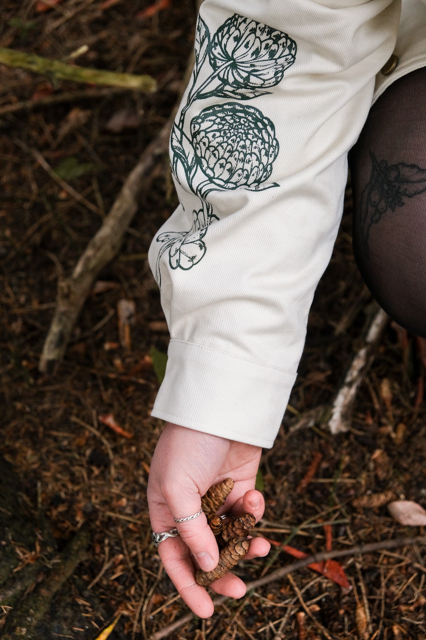 Close up of white better luck next time jacket sleeve cuff, showing part of sleeve dark green floral graphic.