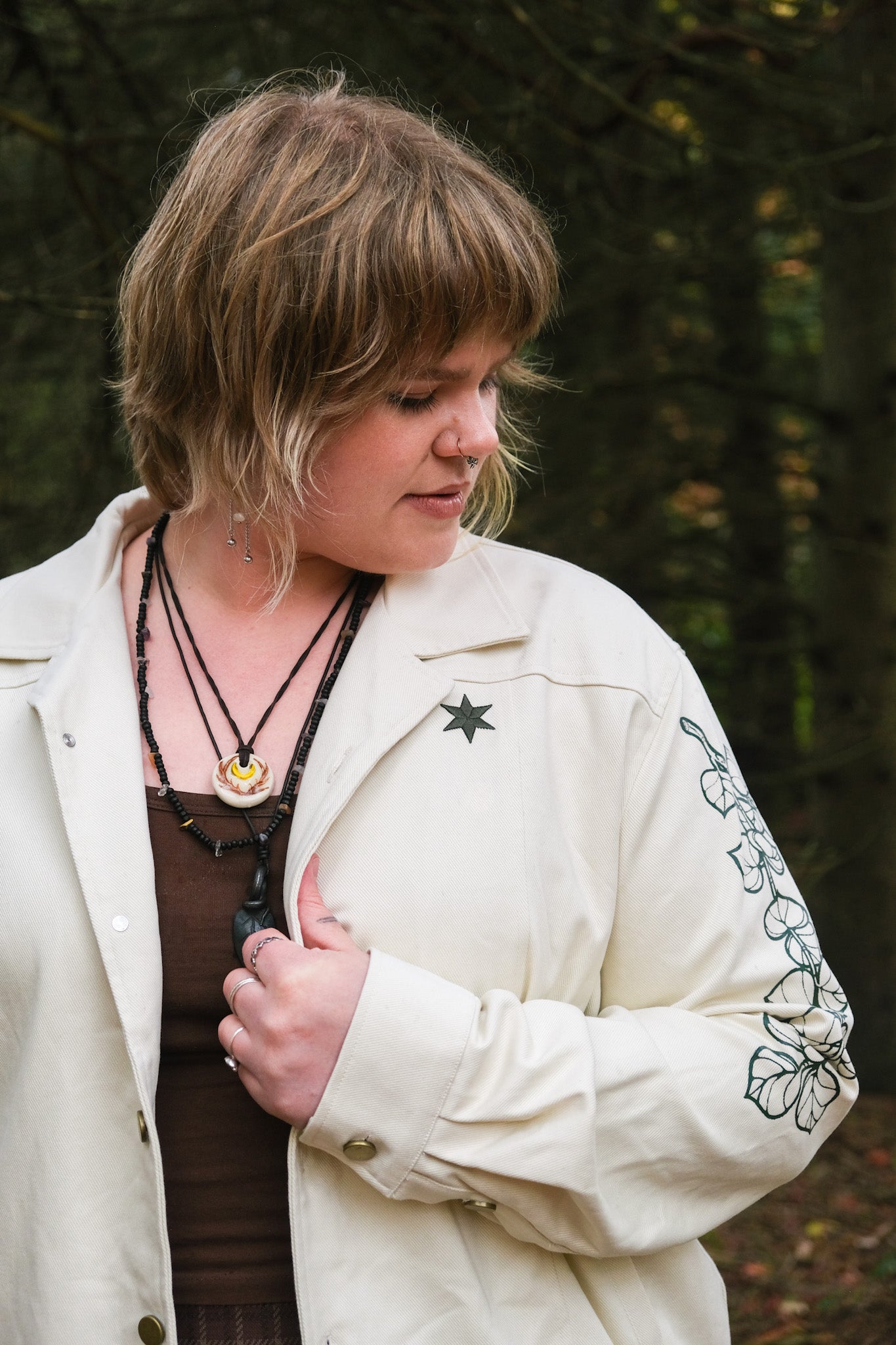 Close up of woman wearing white better luck next time jacket in size extra large showing green leaf graphic on sleeve and green star on jacket front panel.