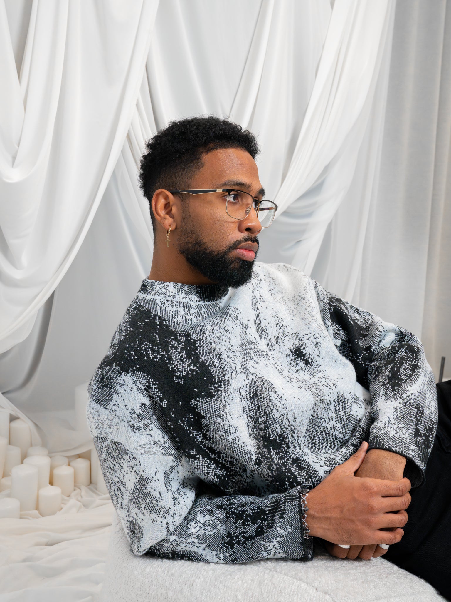 Man posing on ground wearing white, grey and black cropped knit lunar sweater in size large.