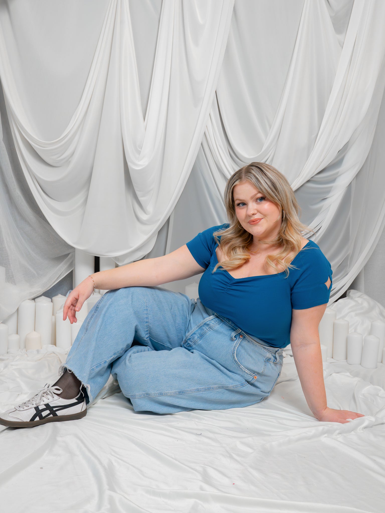 Woman sitting on white fabric wearing blue moon (blue) cap sleeve tee with blue jeans.