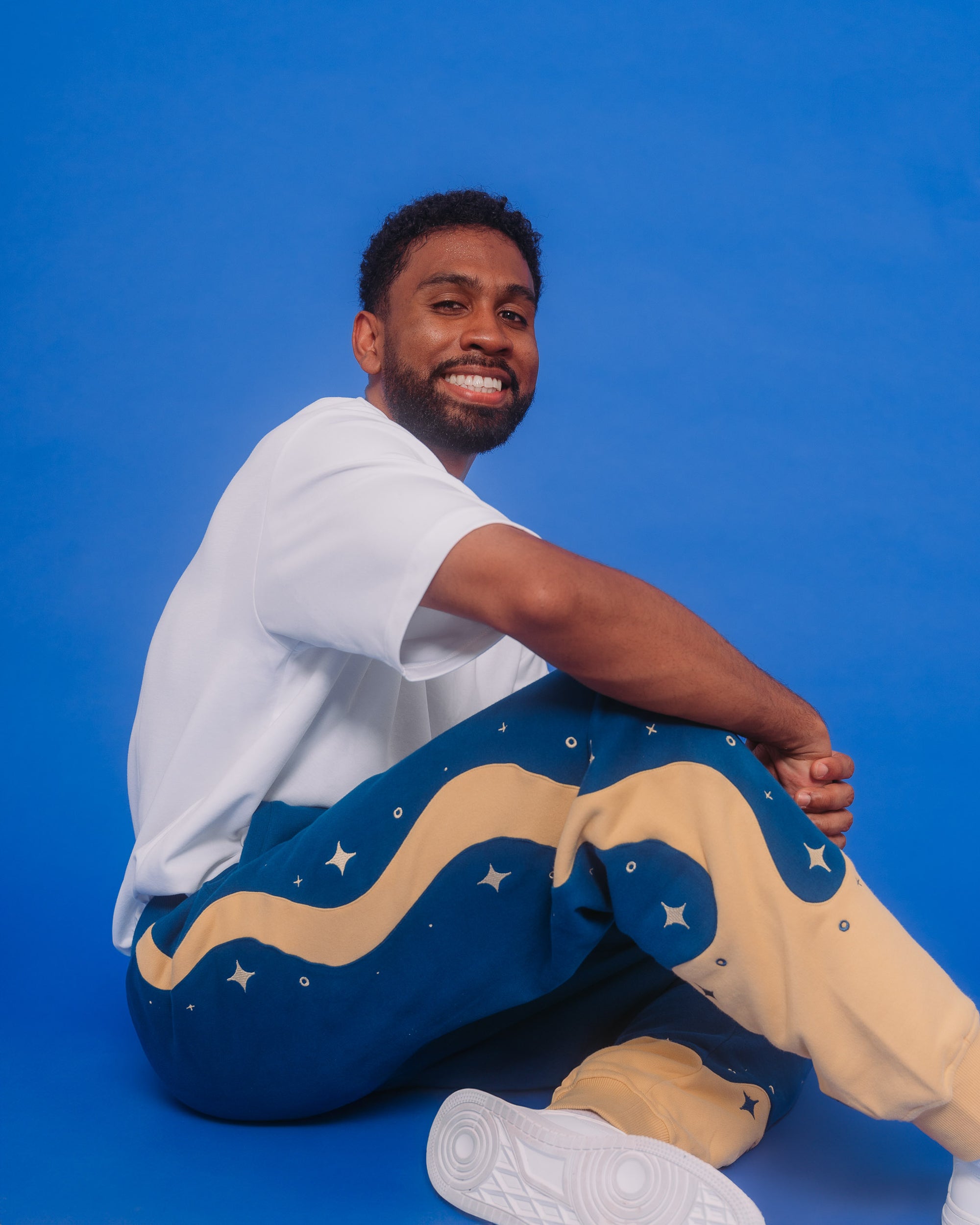 Man wearing blue moon joggers in size large sitting on ground in front of blue background.