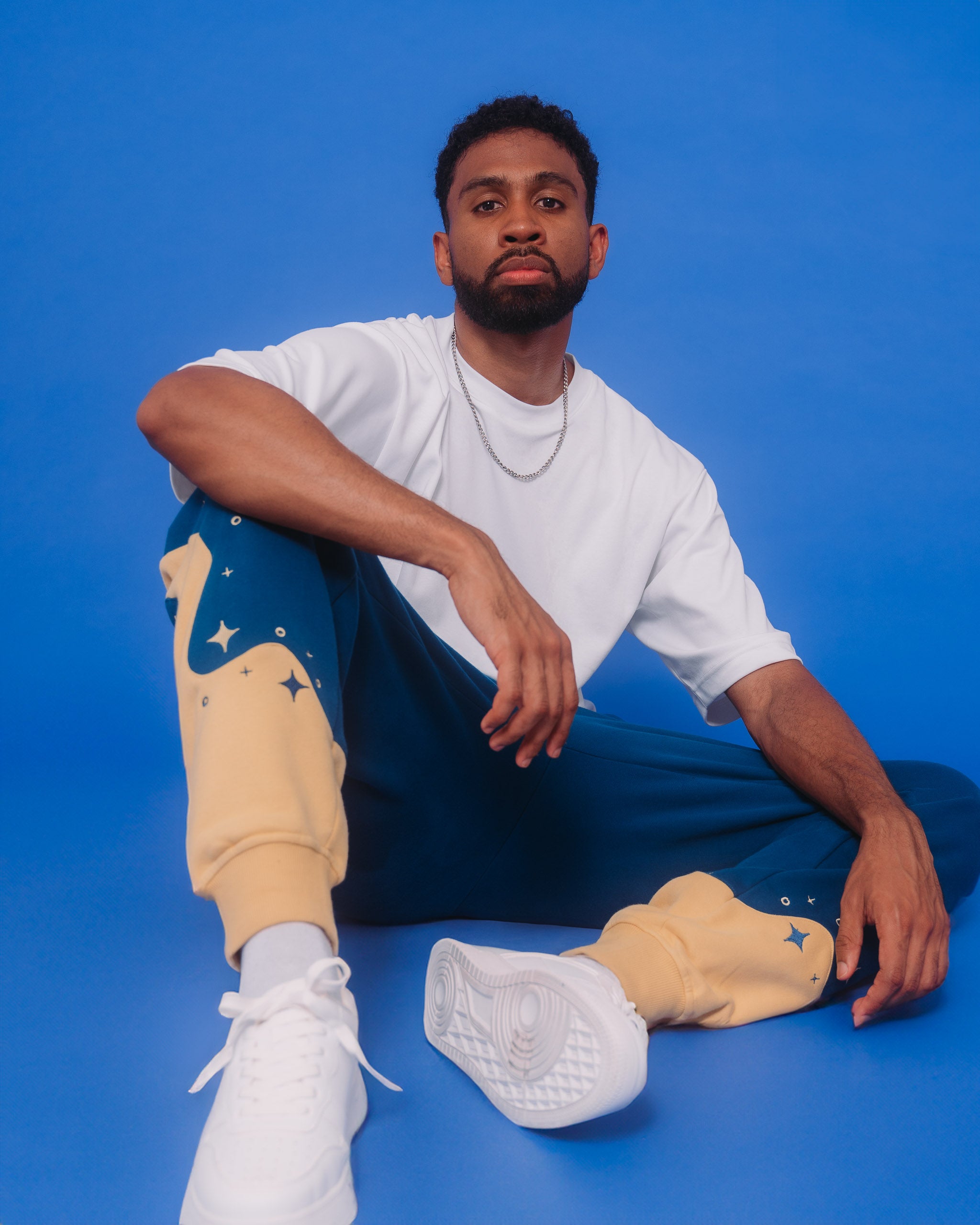 Man wearing blue moon joggers in size large sitting on ground in front of blue background.