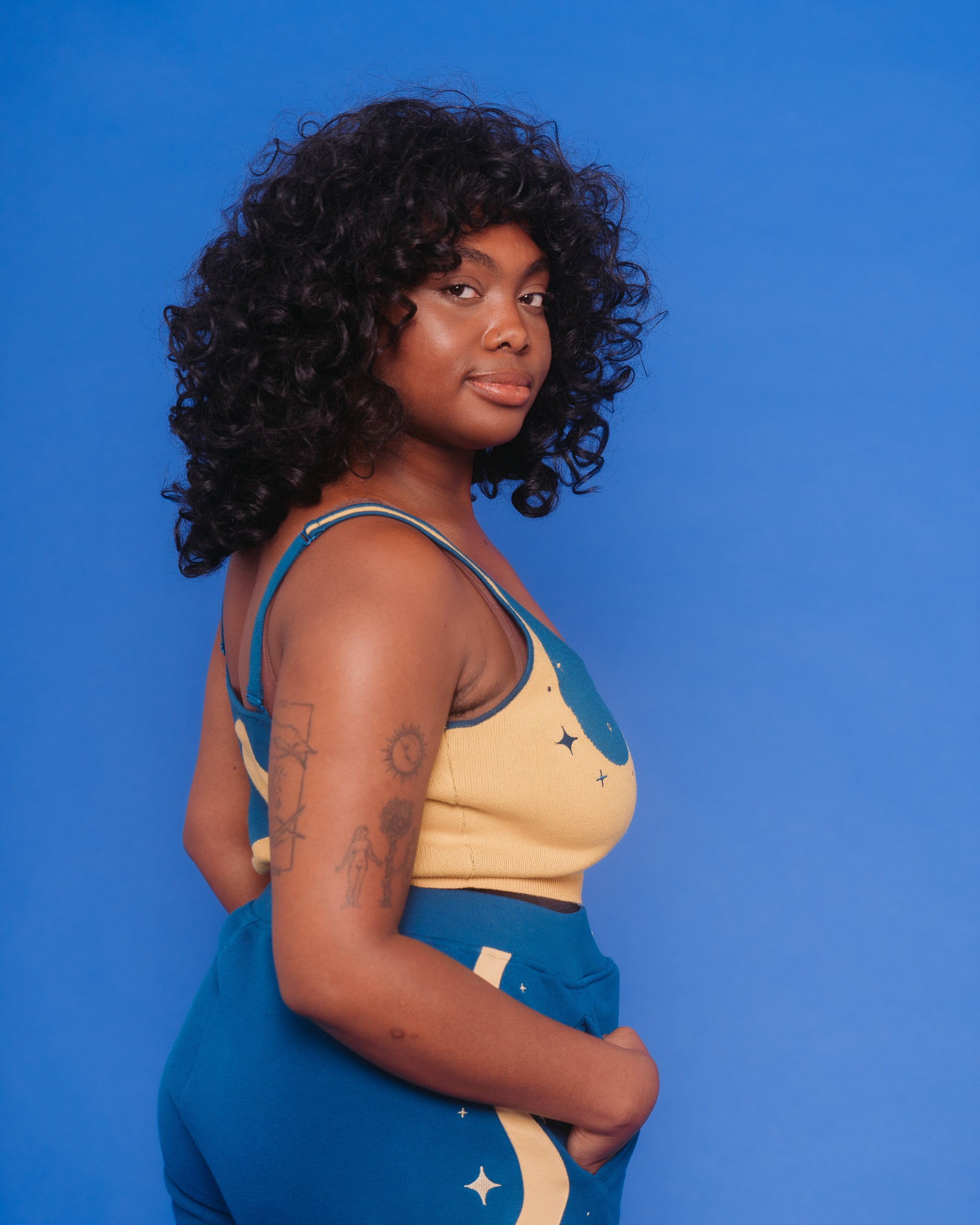 Side view of woman wearing blue moon knit tank in size large in front of blue background.