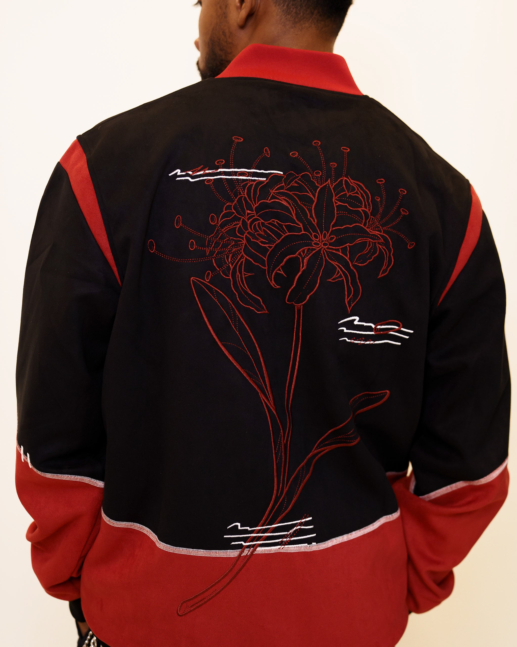 Back view of calling card faux-suede jacket showcasing red spider lily flower embroidery and white jagged lines embroidery.