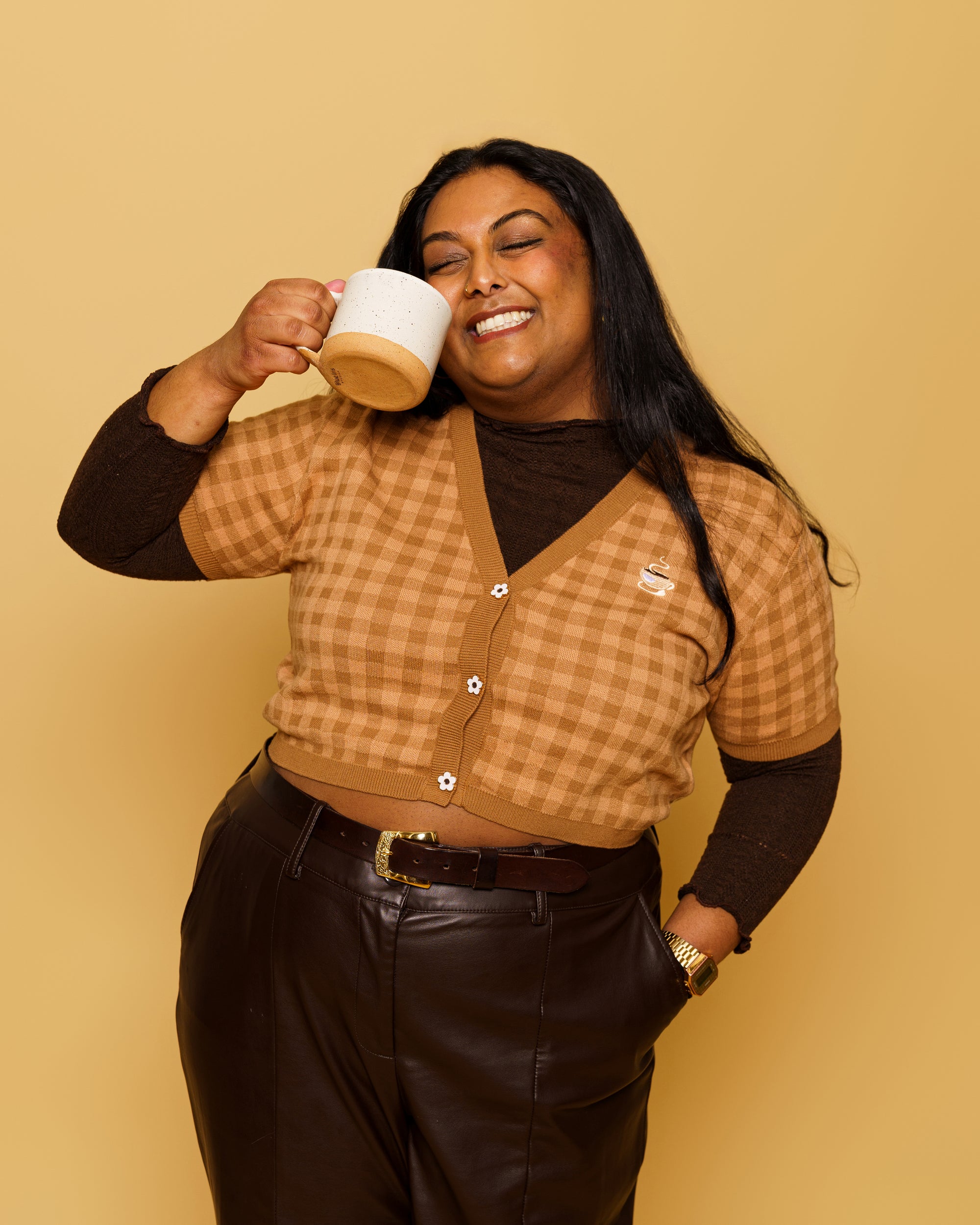 Woman wearing cappuccino mini cardigan in size 3XL holding a mug in front of soft yellow background.