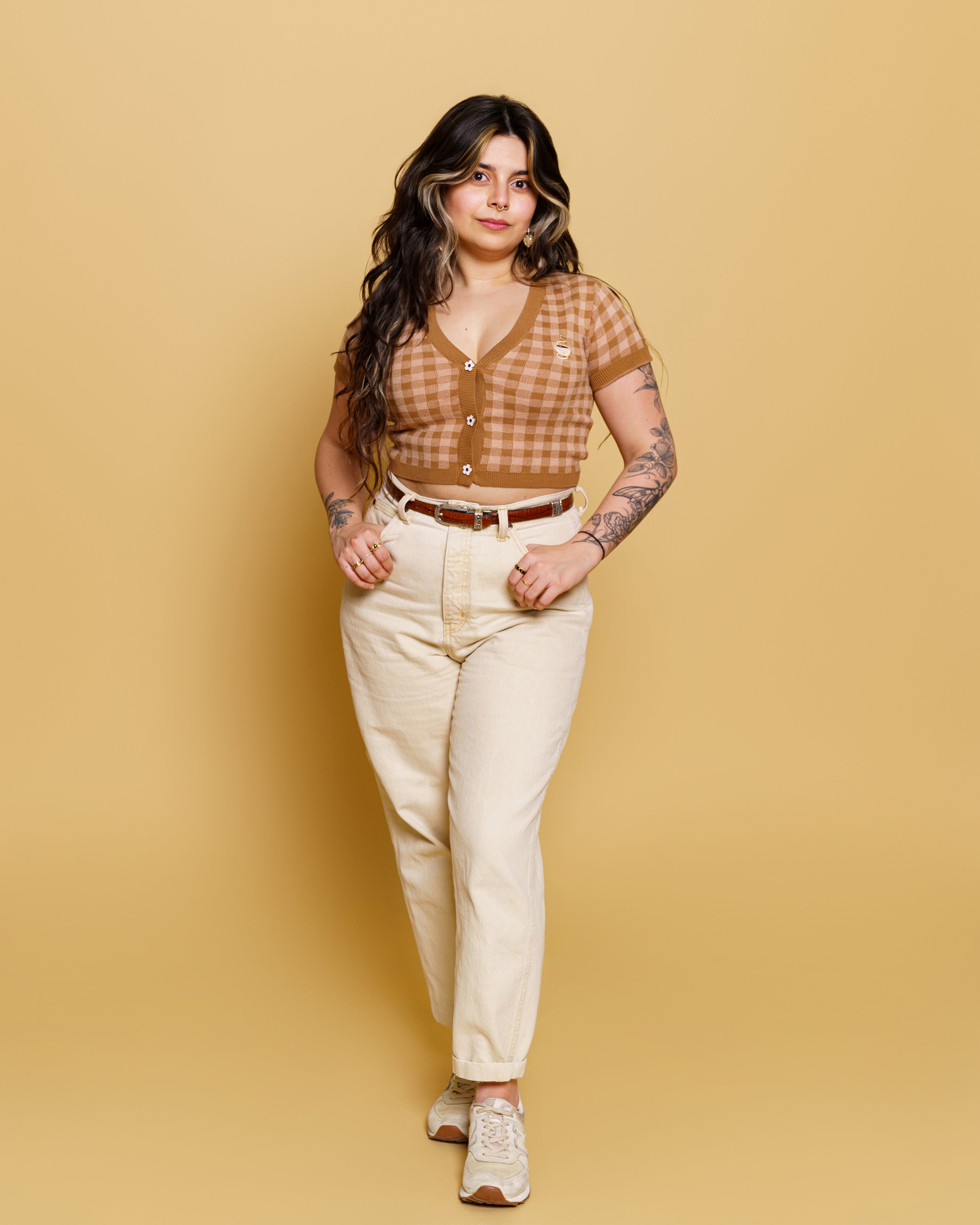 Woman wearing cappuccino mini cardigan in size medium with off-white pants in front of soft yellow background.