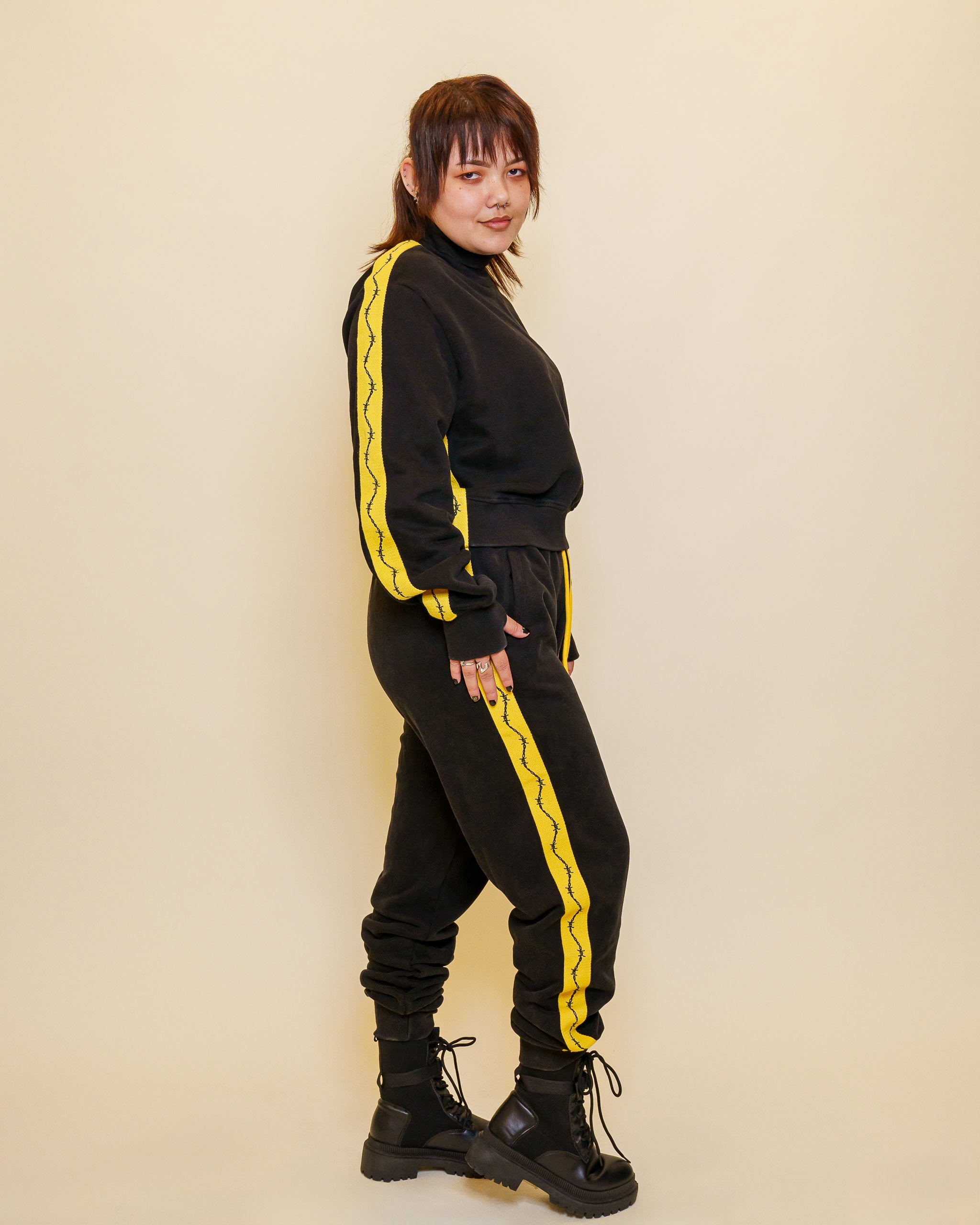 Woman wearing caution cropped mock neck sweater standing to the side showing barbed wire sleeve detail.