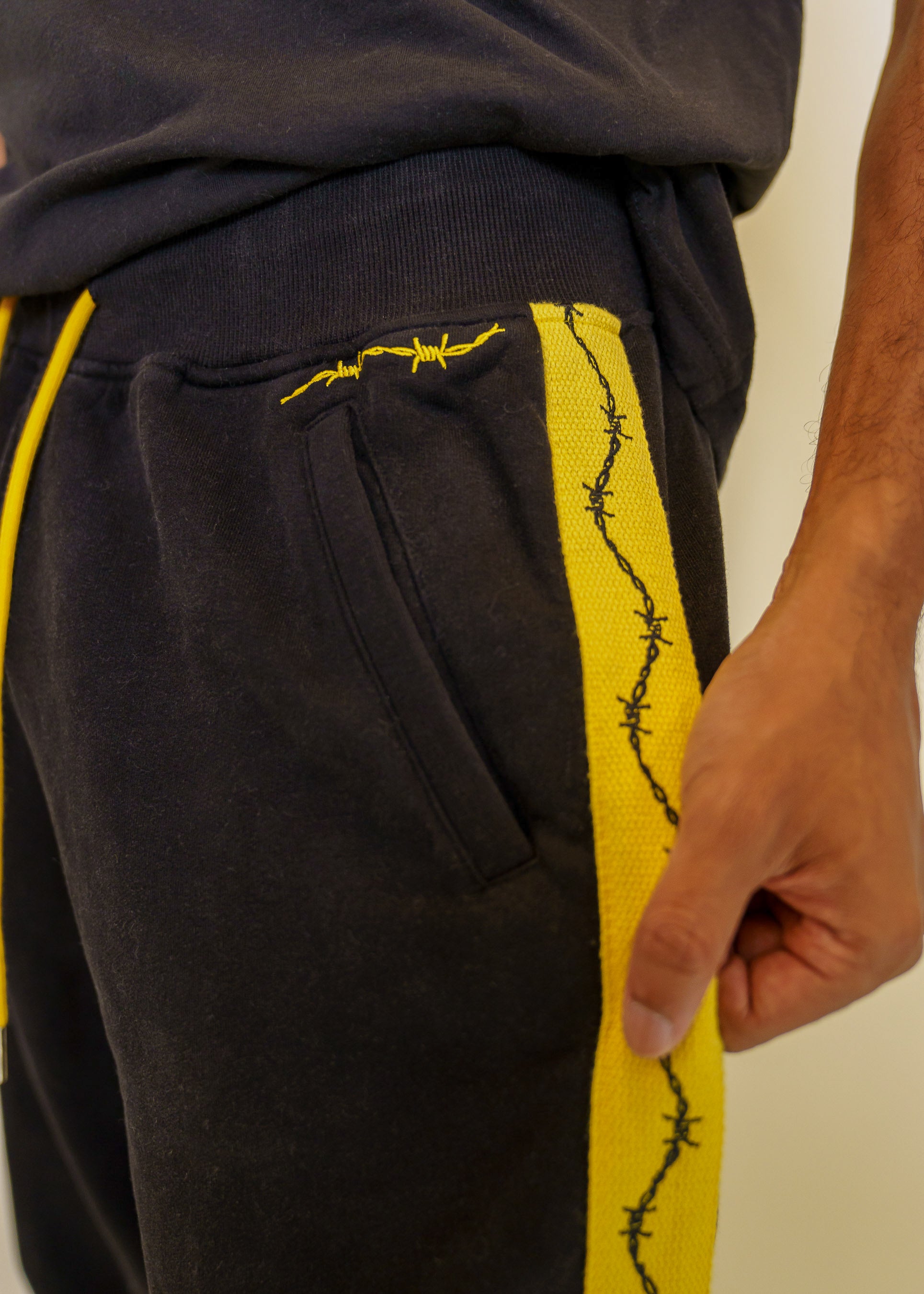Close up of caution joggers yellow side stripe detail with black barbed wire graphic going downwards.