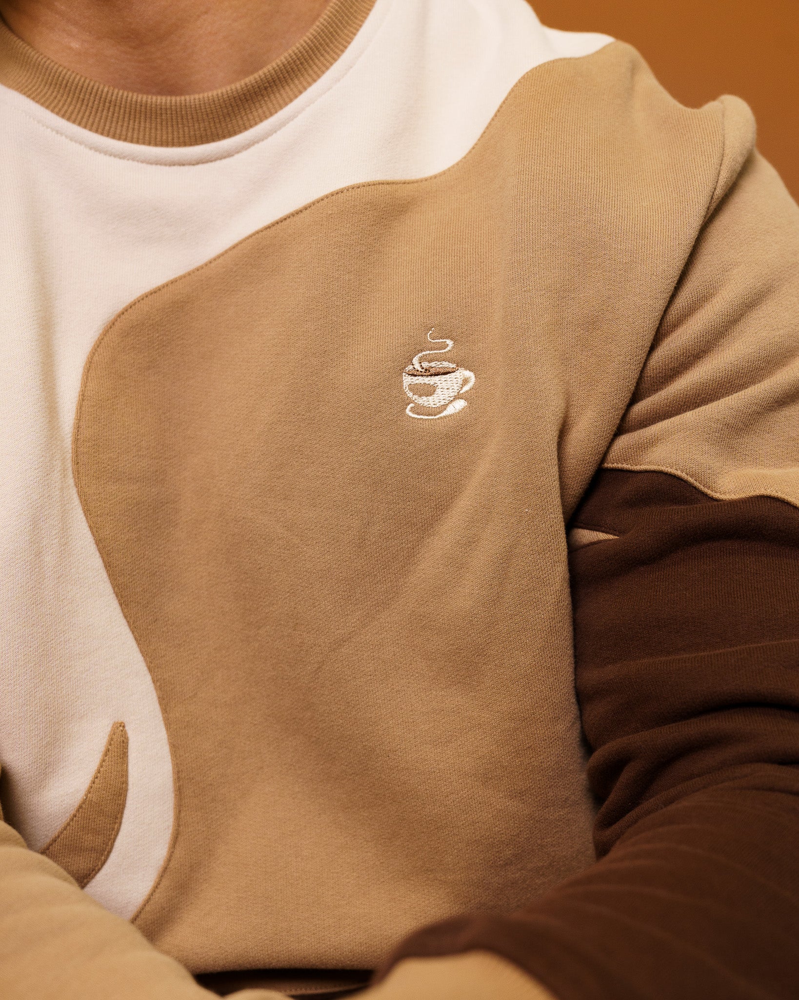 Close up of brown and white cold-brew crewneck embroidered coffee design on chest.