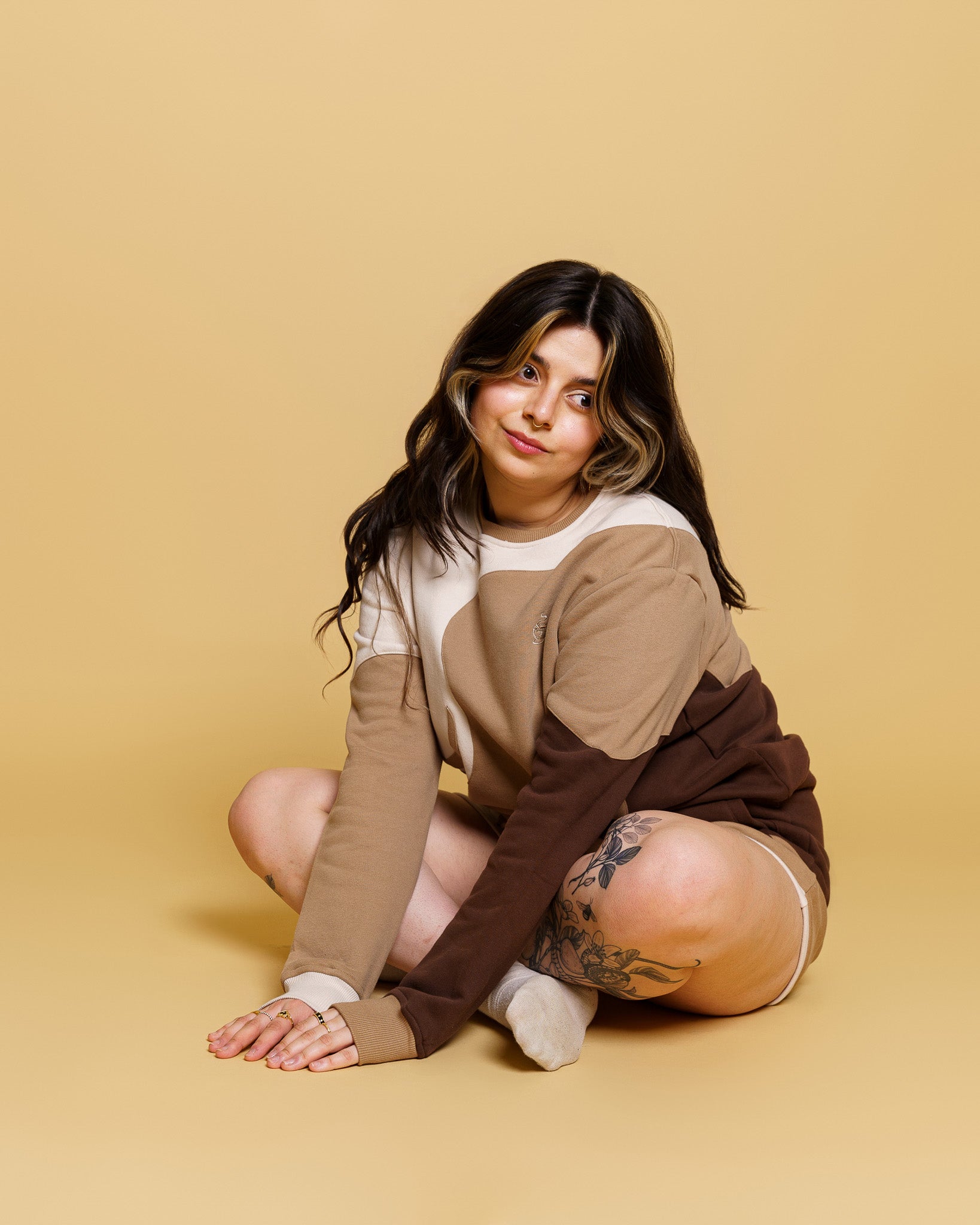 Woman wearing cold-brew crewneck in size small with cold-brew shorts sitting on ground in front of yellow background.