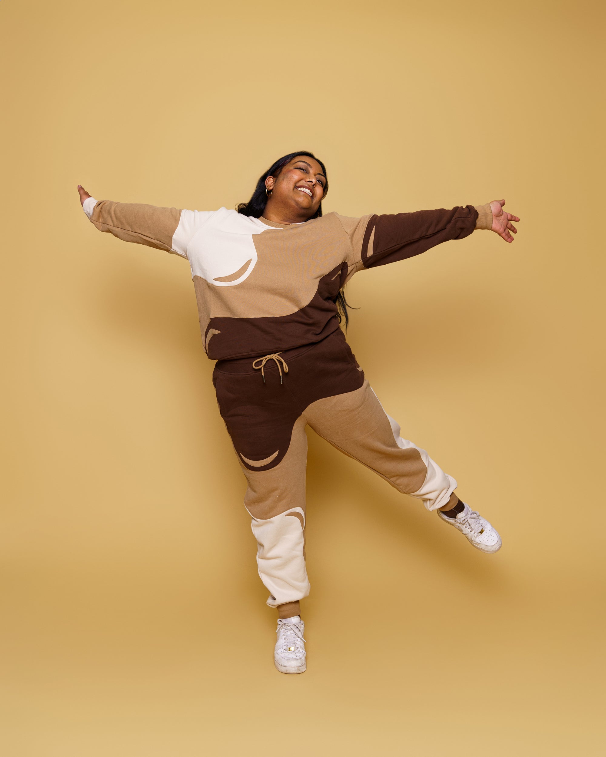 Woman wearing cold brew jogger pants in size 3XL jumping into the air in front of soft yellow background.
