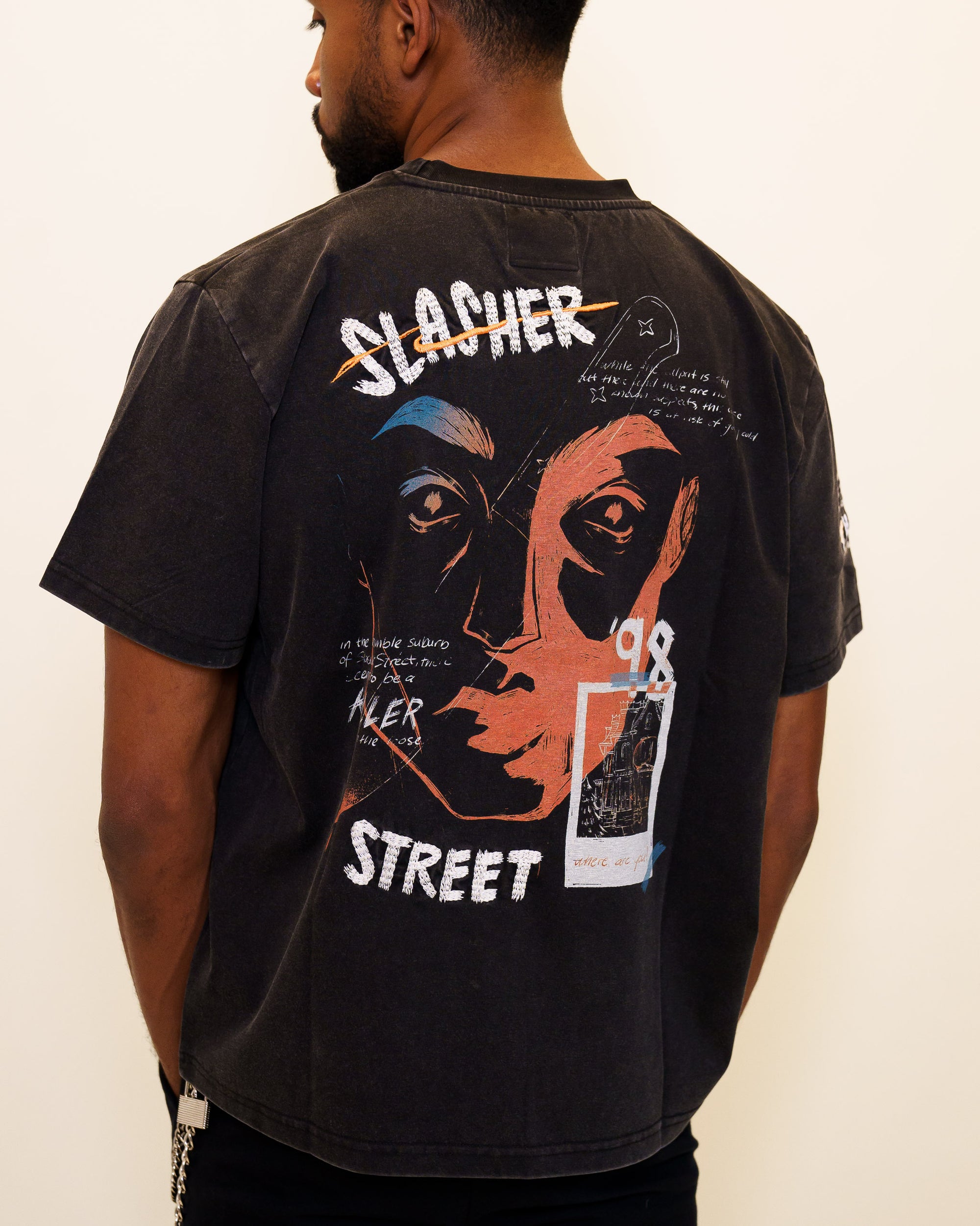 Back view of man wearing cold case tee in size 46 showcasing back graphic featuring embroidered text, screen-printed face, photograph, and knife. 