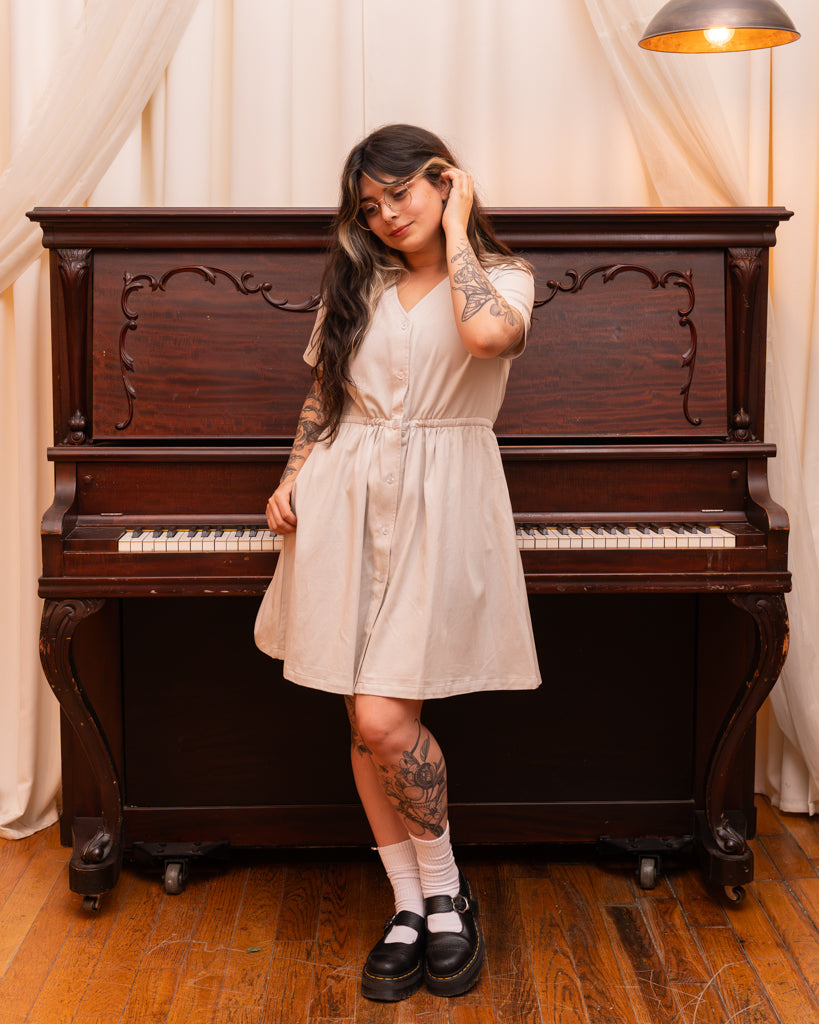 Front view of woman wearing curtsy white smock dress in size small in front of piano.