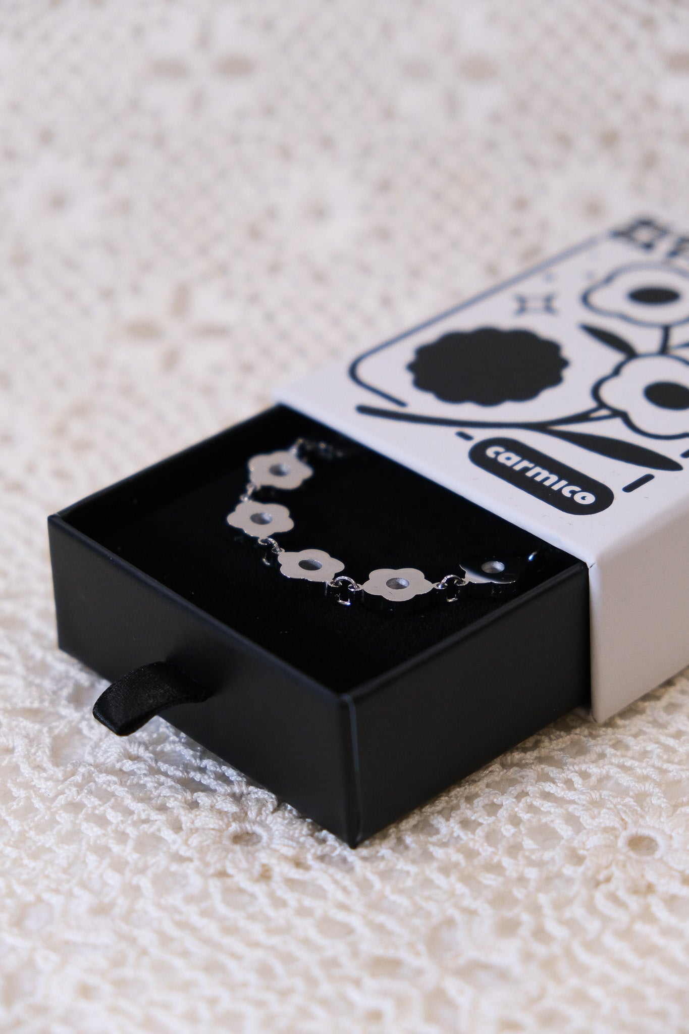 Silver daisy chain necklace sitting inside of its drawer style packaging.