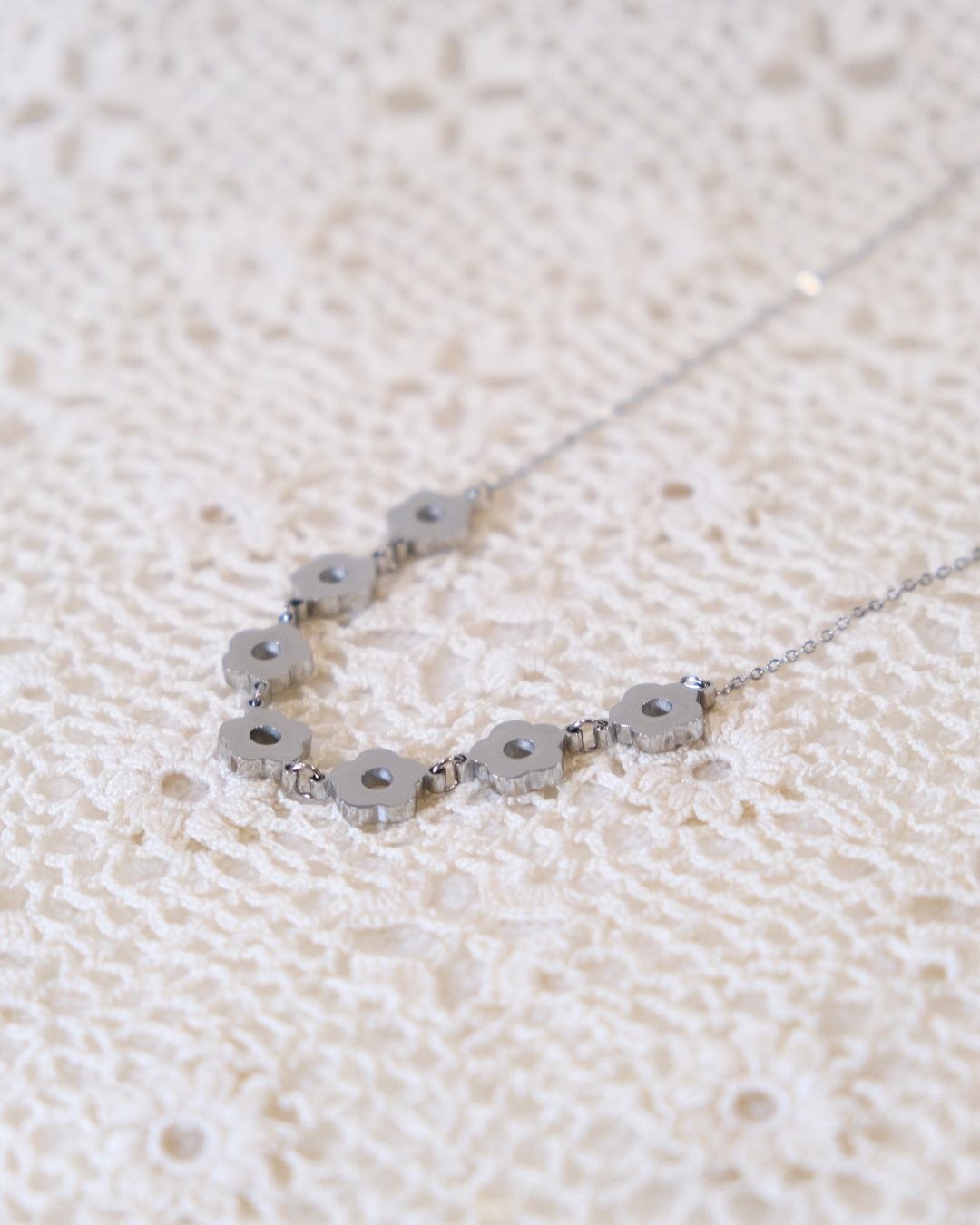 Silver daisy chain laying on white lace.