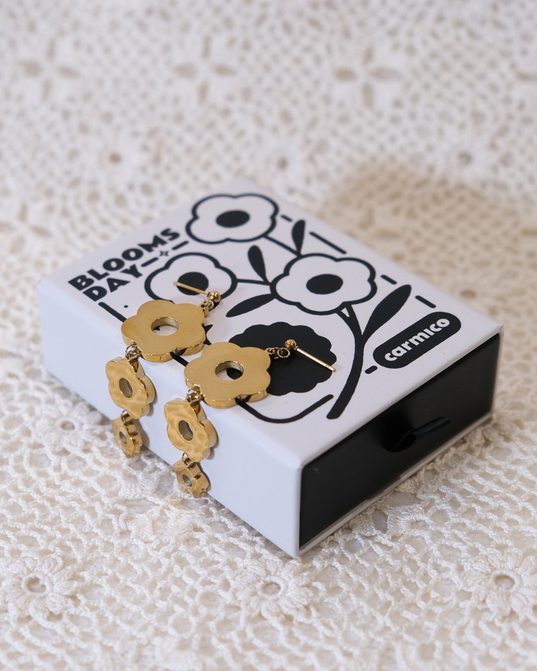 Golden daisy dangle earrings sitting on box.