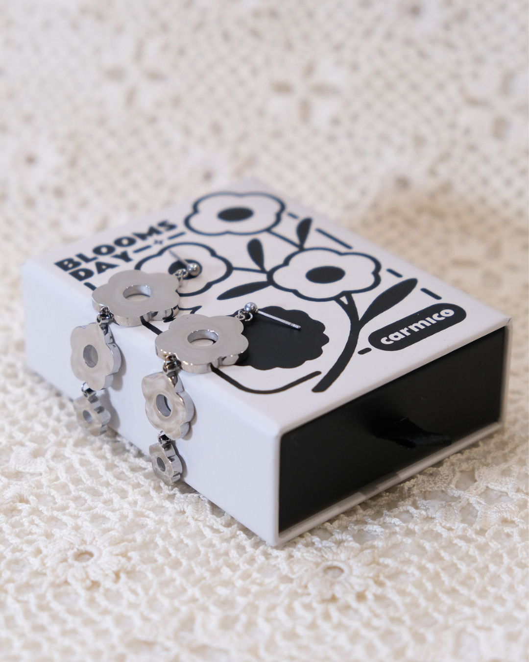 Silver daisy dangle earrings sitting on box.