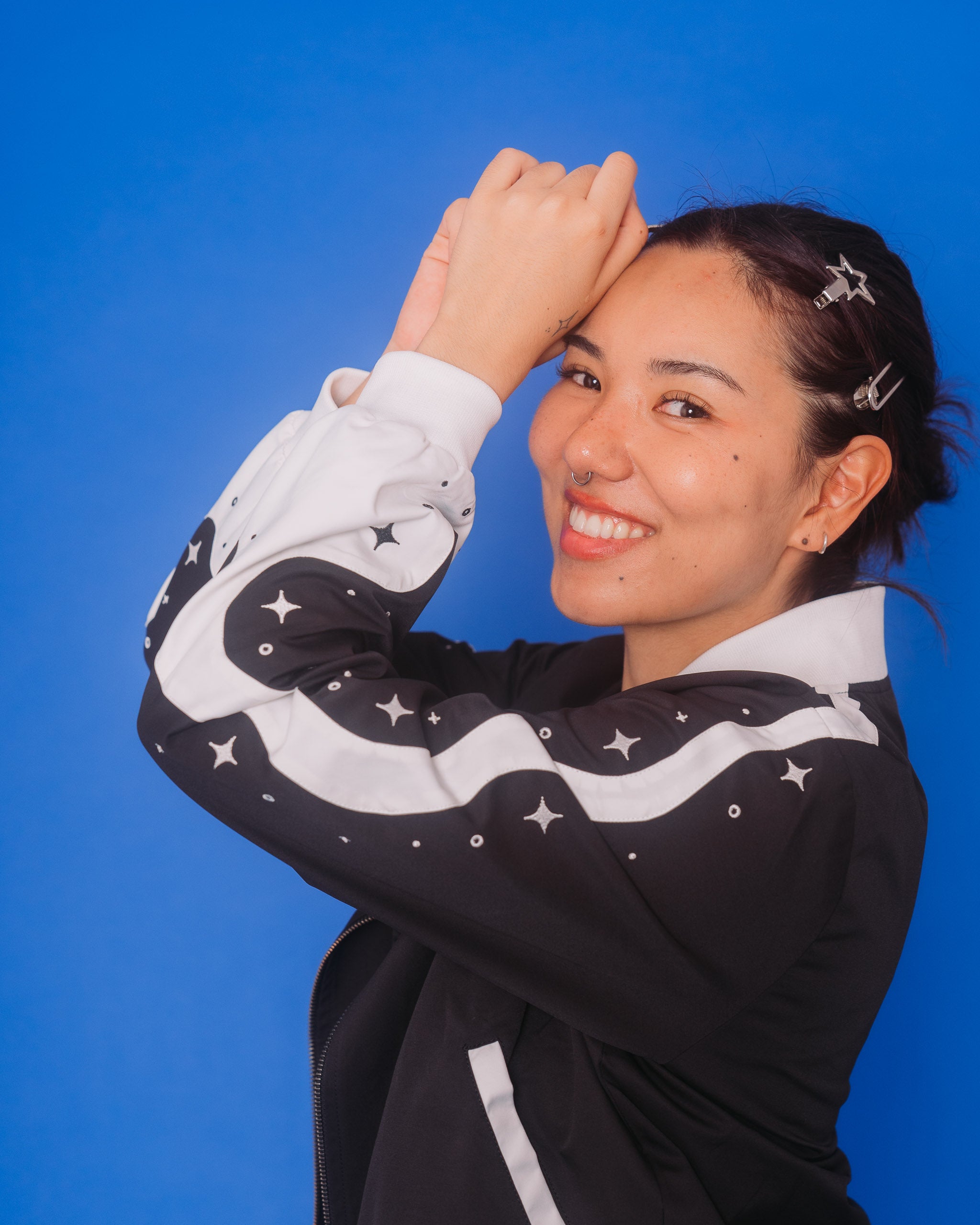 Woman wearing deep space bomber jacket in size medium posing in front of blue background.