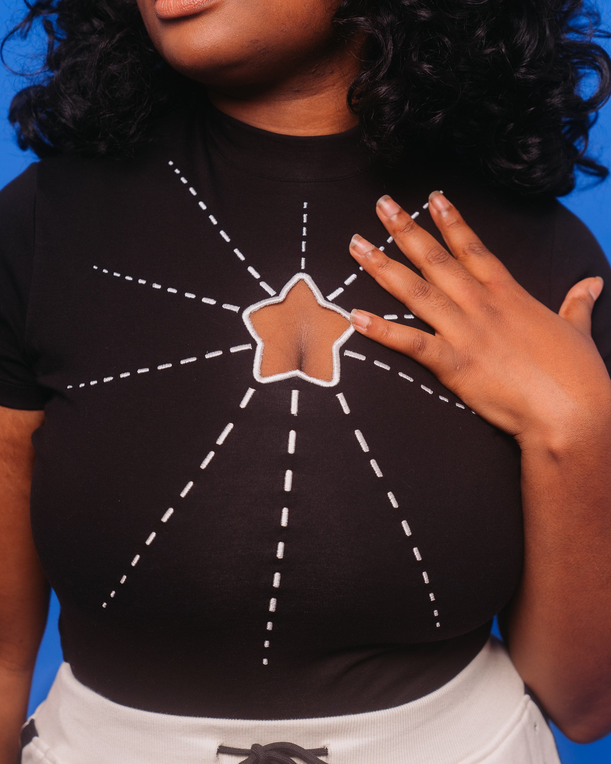 Close up of deep space mini tee showing star cutout and white embroidered lines making a starburst design.