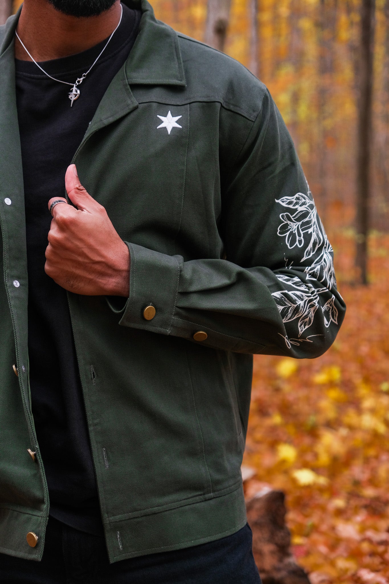 Close up of dark green don't cross me jacket showing white floral design on sleeve and white star on jacket front panel.
