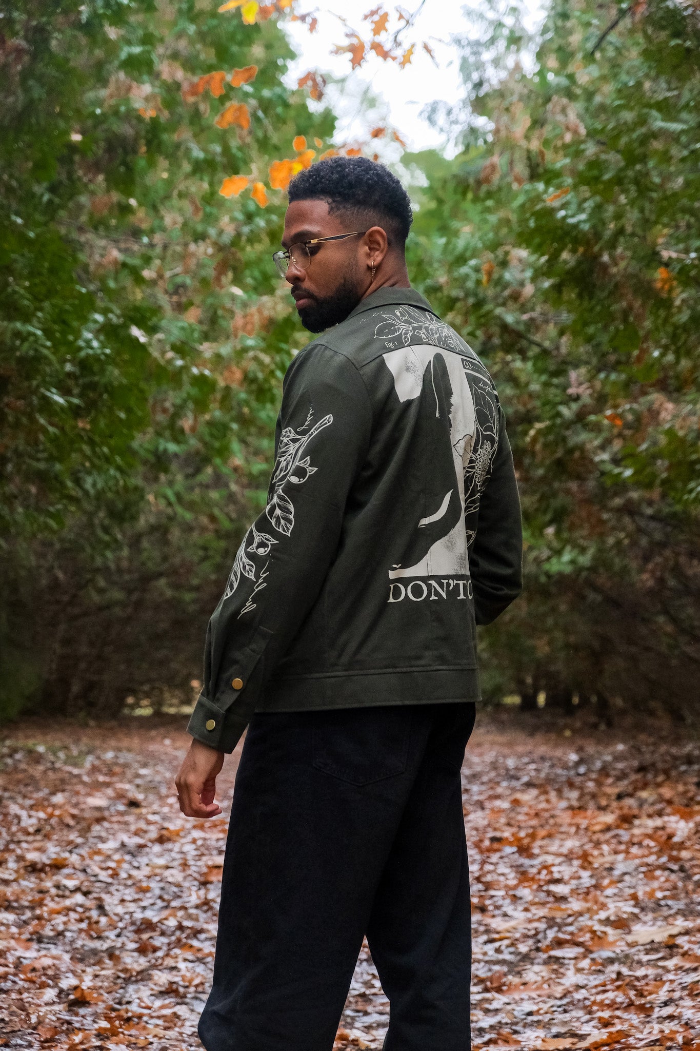 Man wearing dark green don't cross me jacket in size large looking over the shoulder in forest.