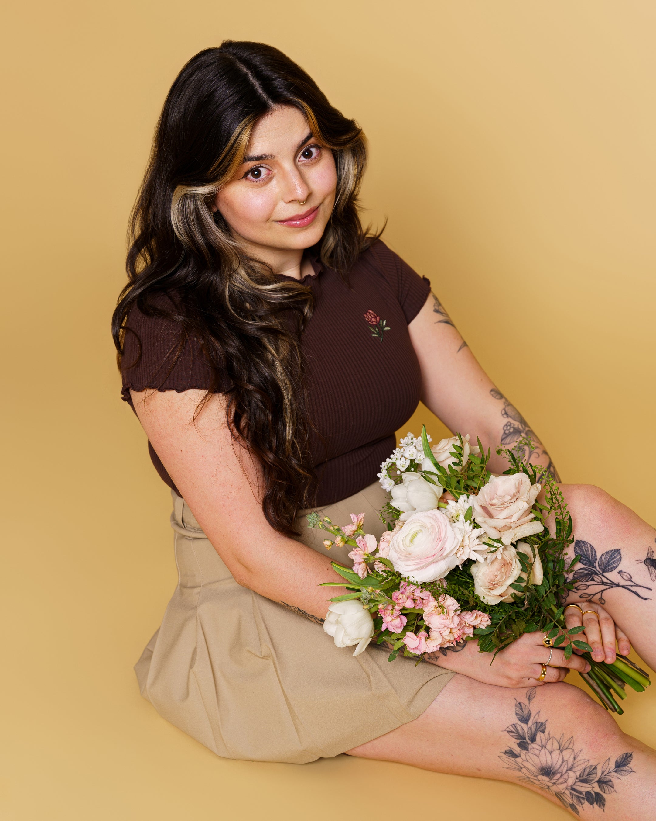 Woman wearing freshly picked brown mini tee in size small holding a bouquet in front of soft yellow background.