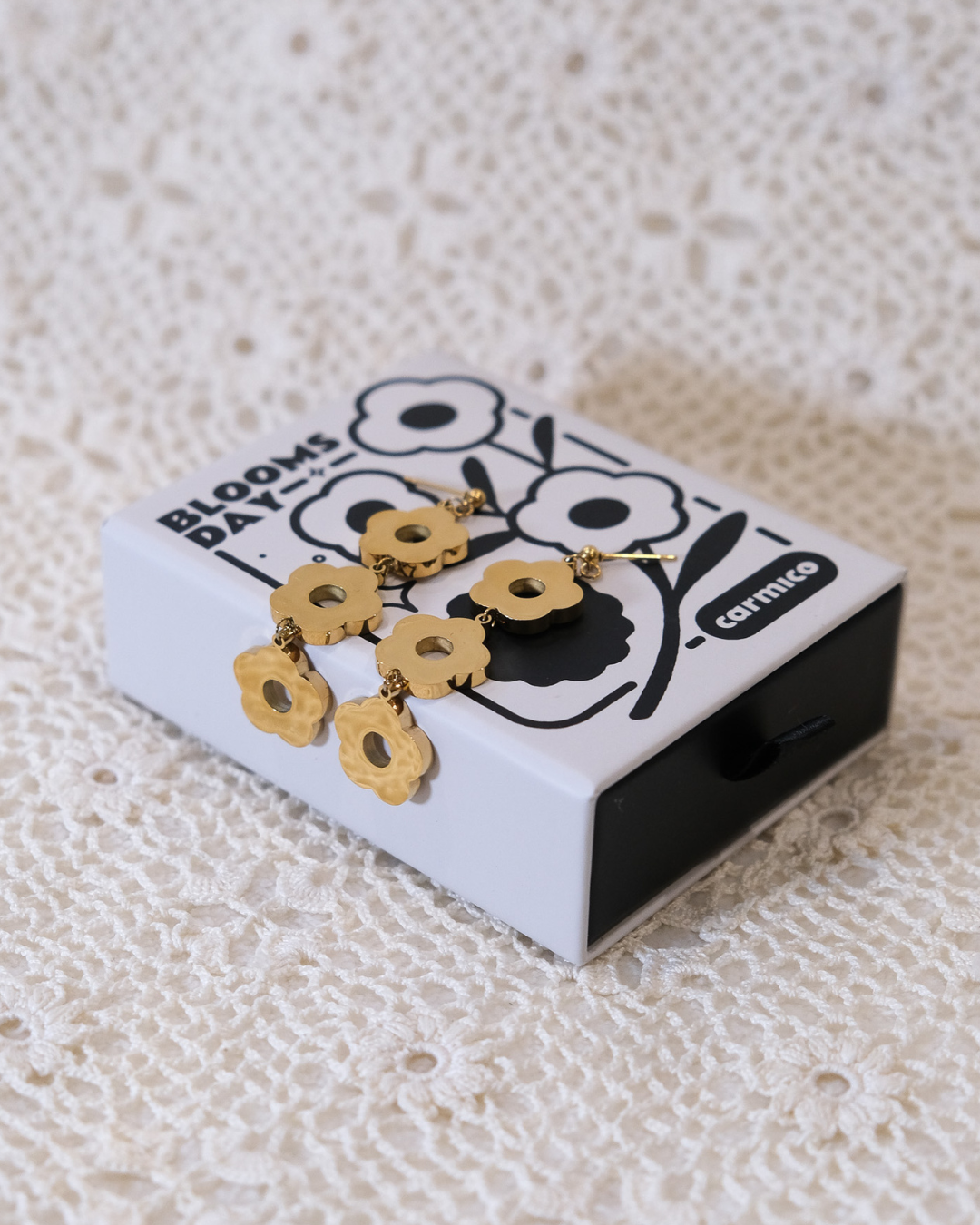 Golden daisy dangle earrings laying on box.