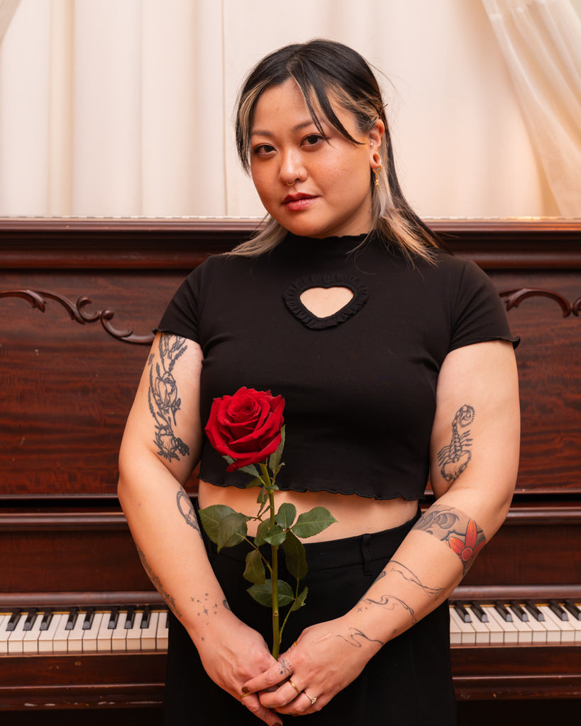Model wearing black heart throb mini tee in size medium holding a red rose.