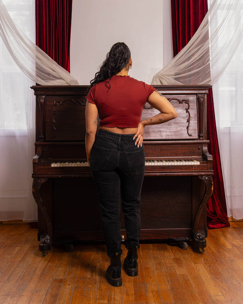 Back view of woman wearing red heart throb mini tee in size small with black pants facing piano.