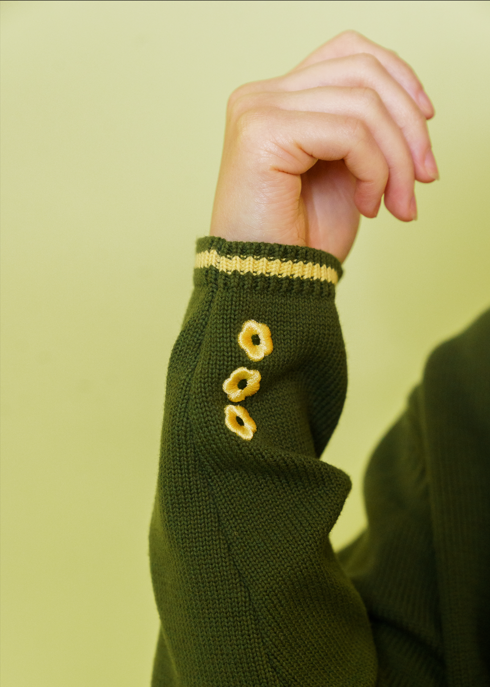 Close up of three yellow embroidered daisy flowers at the cuff of herbal cropped cardigan.