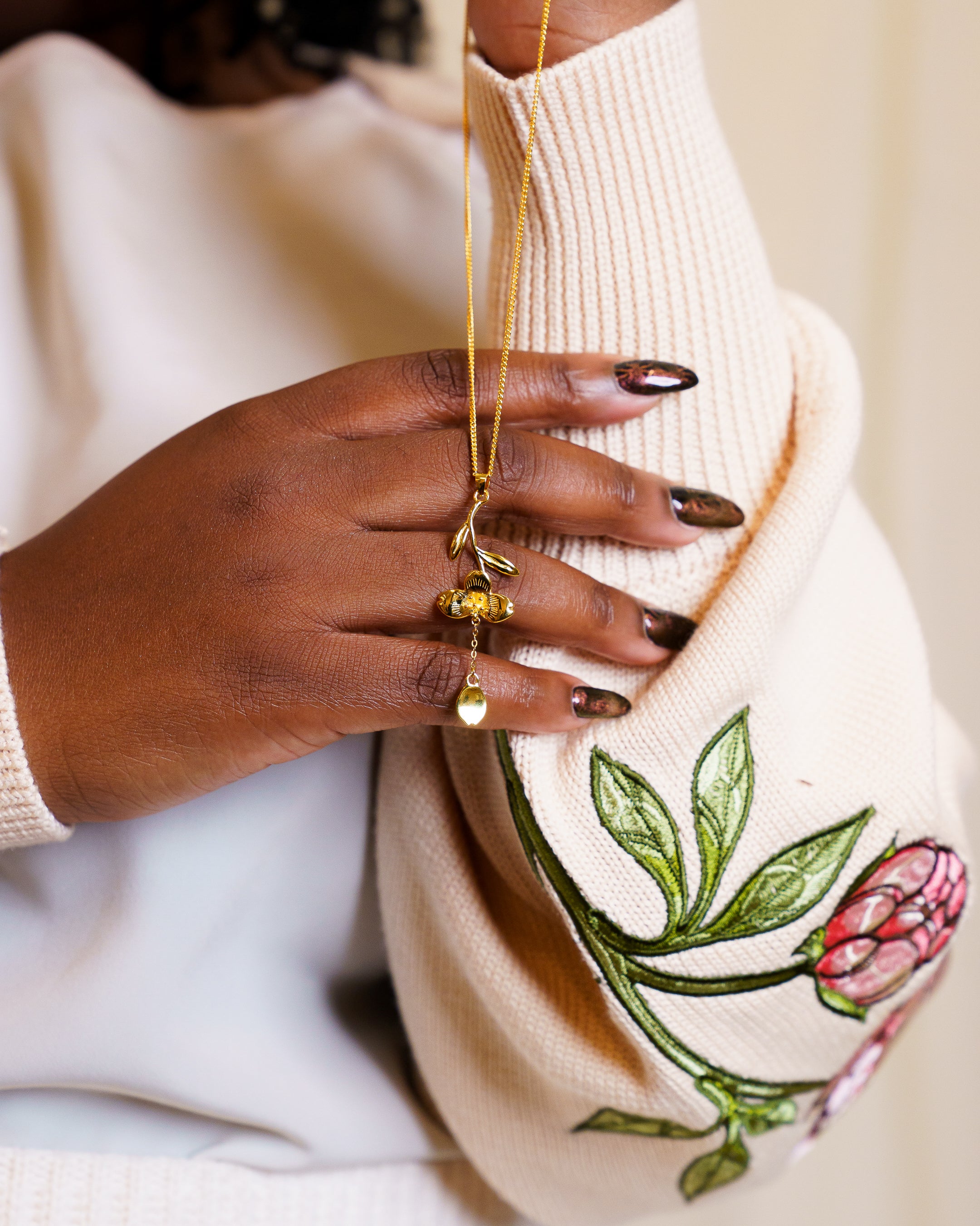 Close up of golden loves me not necklace featuring curved metal stem and dangling petal.