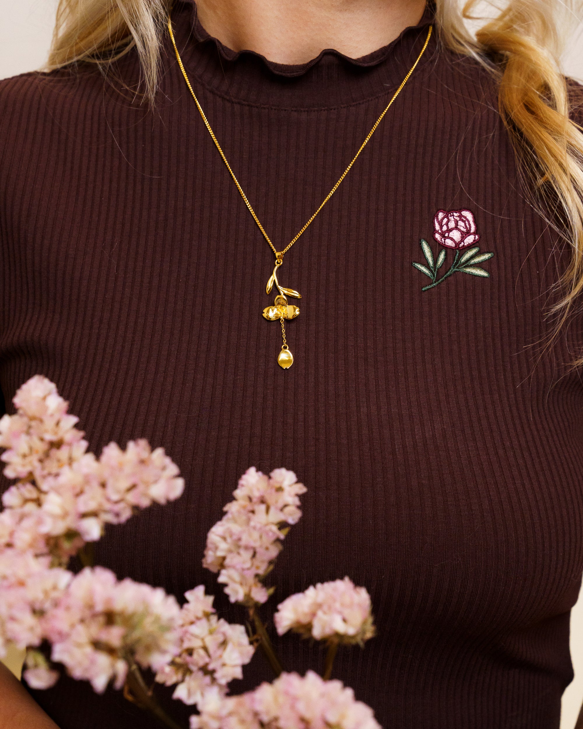 Woman wearing gold loves me not necklace on freshly picked brown mini tee.