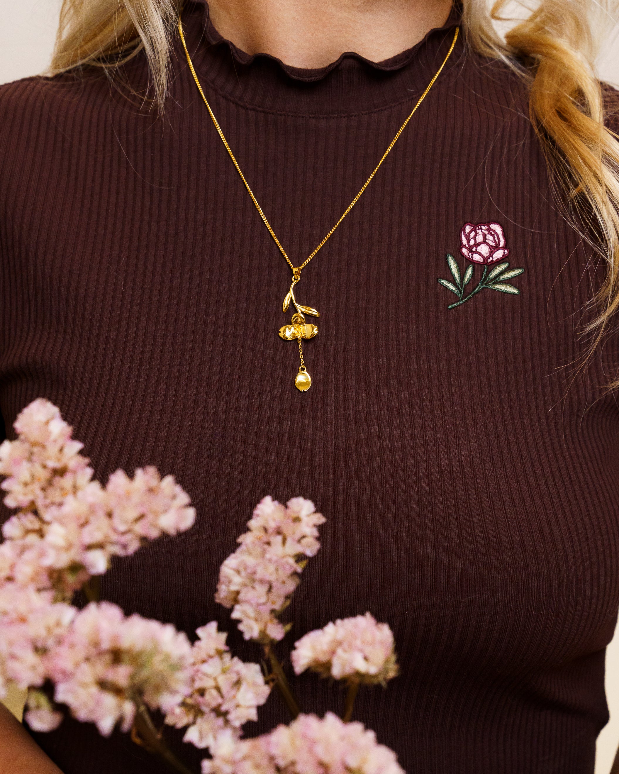 Woman wearing gold loves me not necklace on freshly picked brown mini tee.