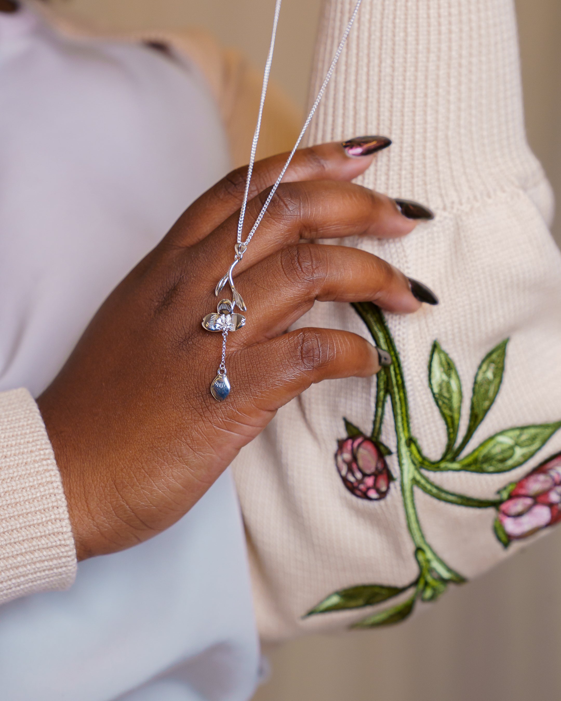 Silver loves me not necklace dangling on hand.