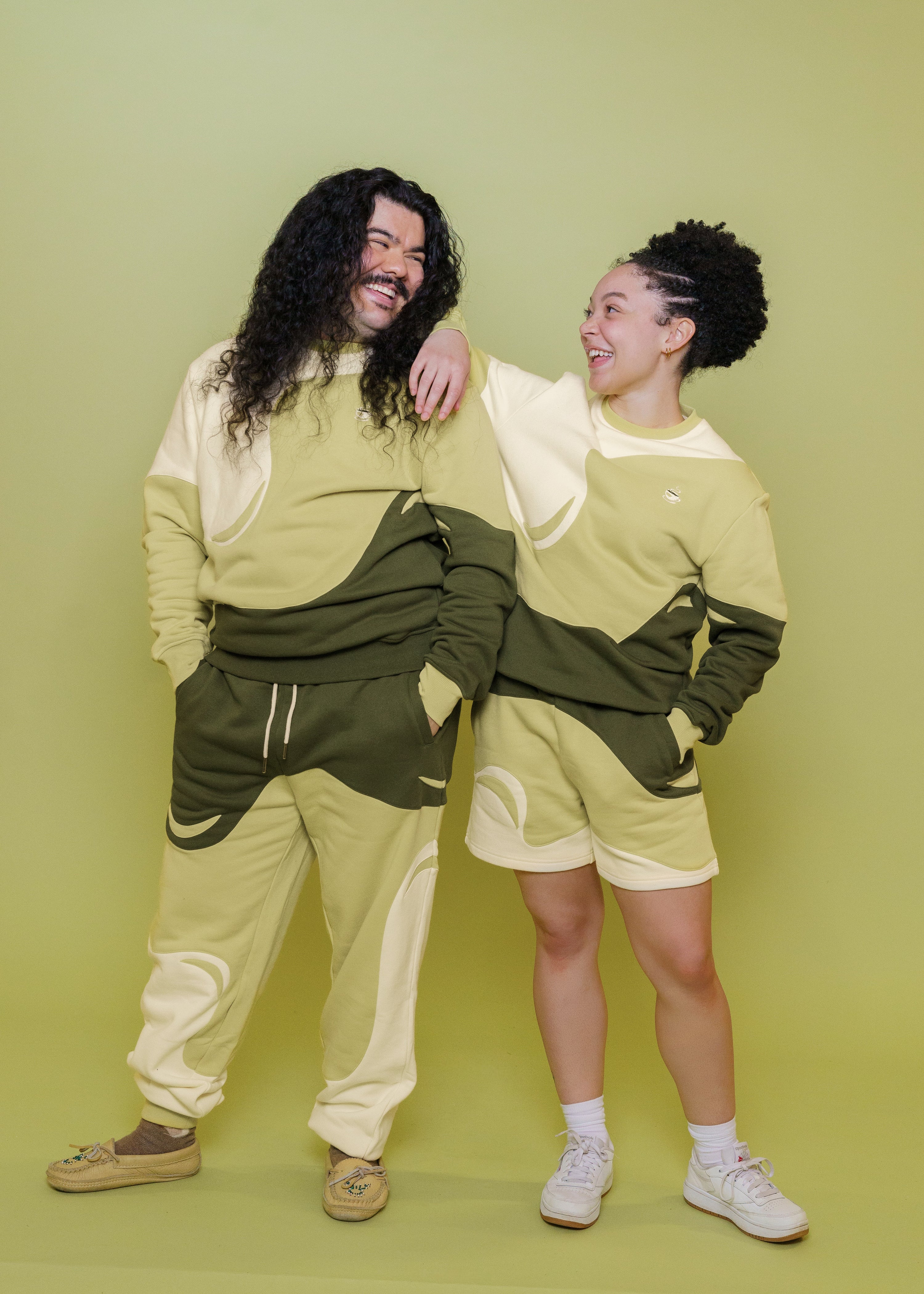 Man and woman wearing monochromatic green matcha crewnecks standing in front of green background.