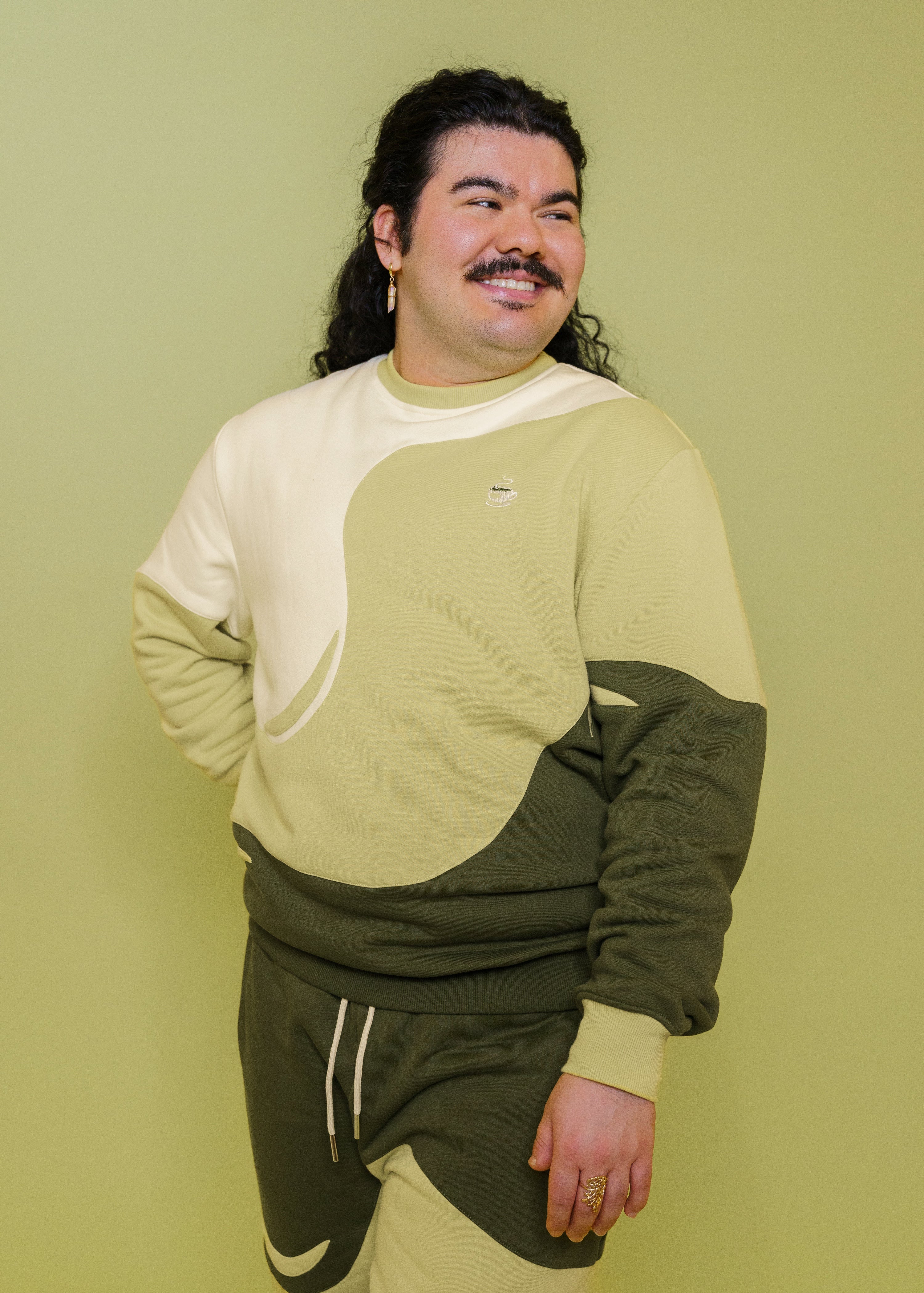 Man wearing monochromatic green matcha crewneck glancing to the side in front of green background.