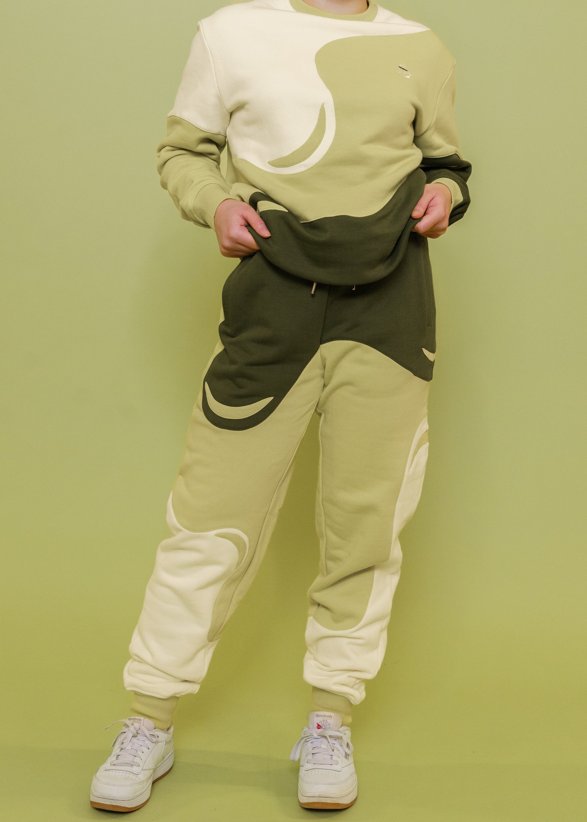 Woman wearing monochromatic green matcha joggers in size extra small with white shoes in front of green background.