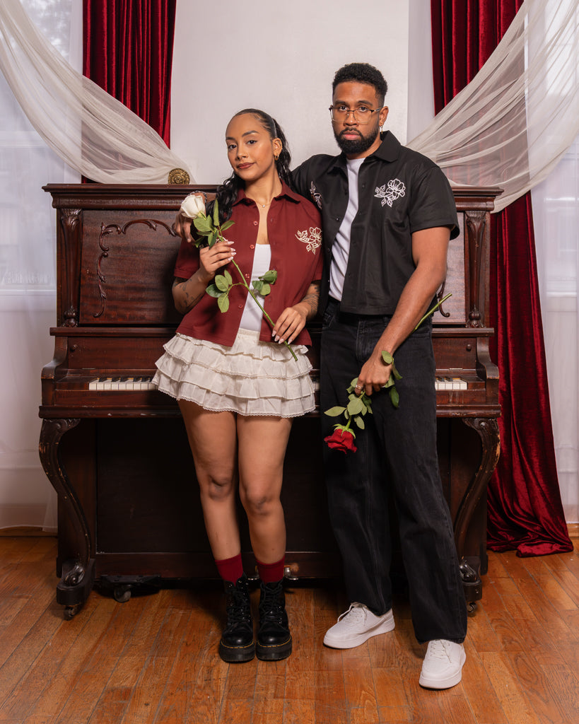 Man wearing mysterious boxy over-shirt in size large standing with arm around woman wearing passionate boxy over-shirt in size small holding roses.