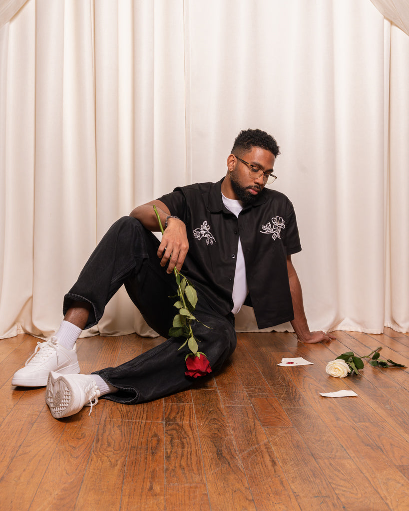 Man wearing mysterious boxy over-shirt in size large sitting on ground with roses and a torn lover letter.