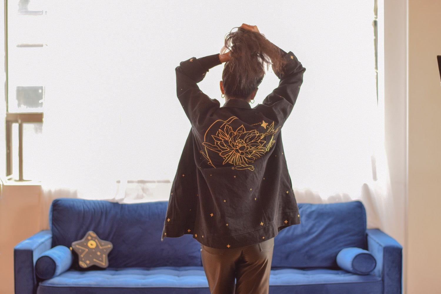 Woman wearing black night bloom jacket  in size small holding hair up showing gold embroidered moon and flower on back of jacket.