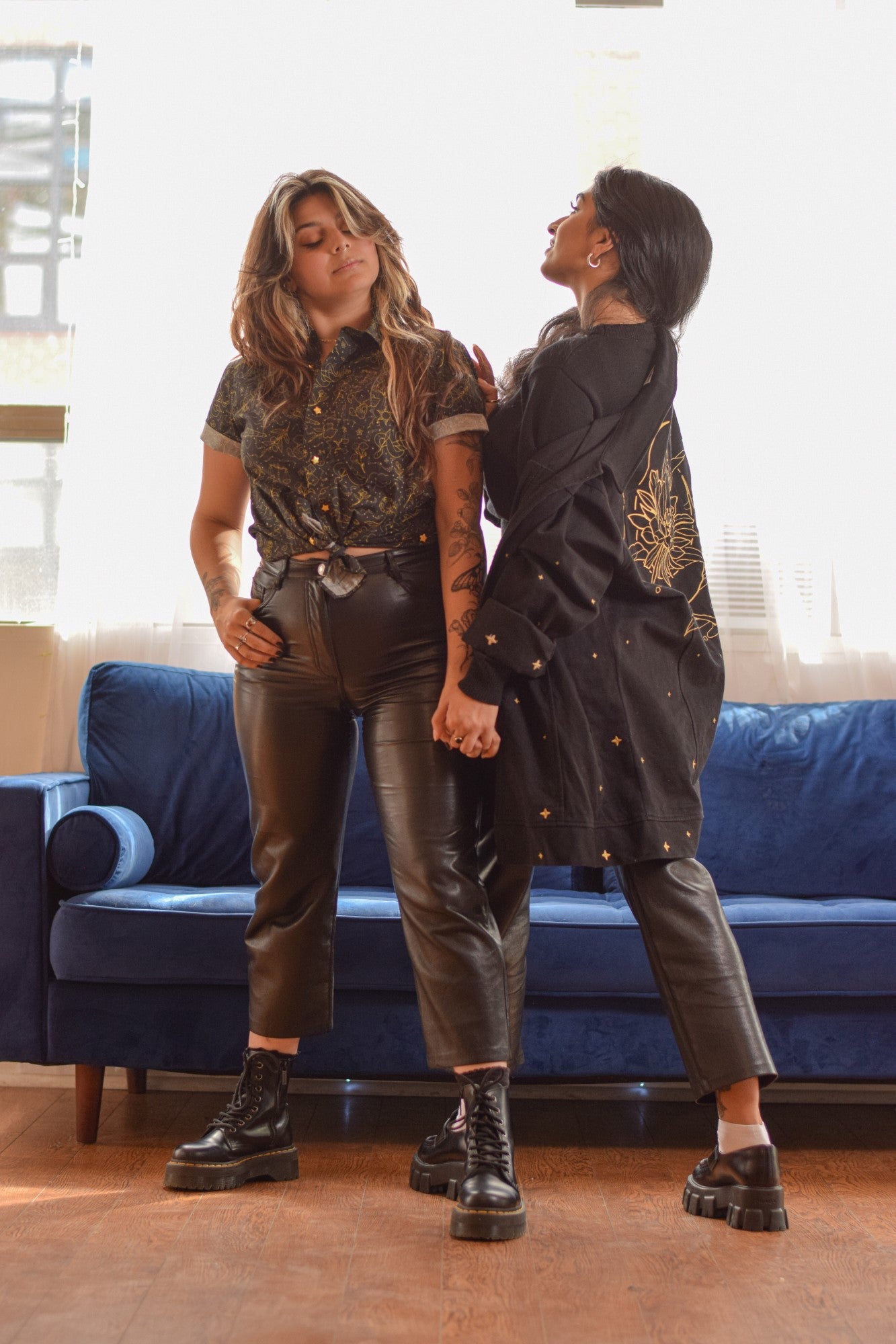 Two women standing together with one wearing black night bloom jacket in size small facing back towards camera and the other wearing black nightfall button up shirt in size small facing the camera.