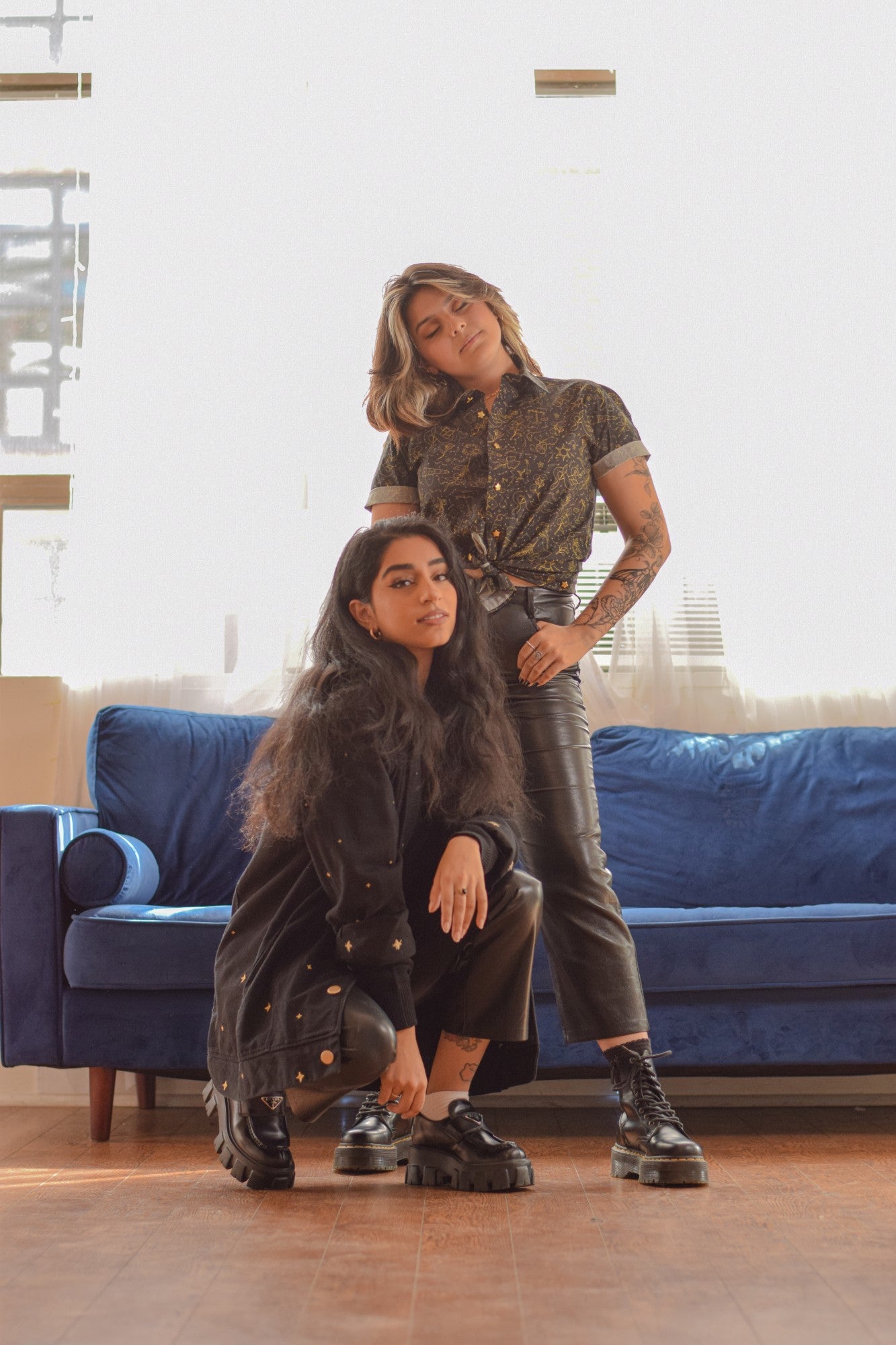 Two women facing camera, one standing wearing black nightfall button up in size small and the other crouched down wearing black night bloom jacket in size small.