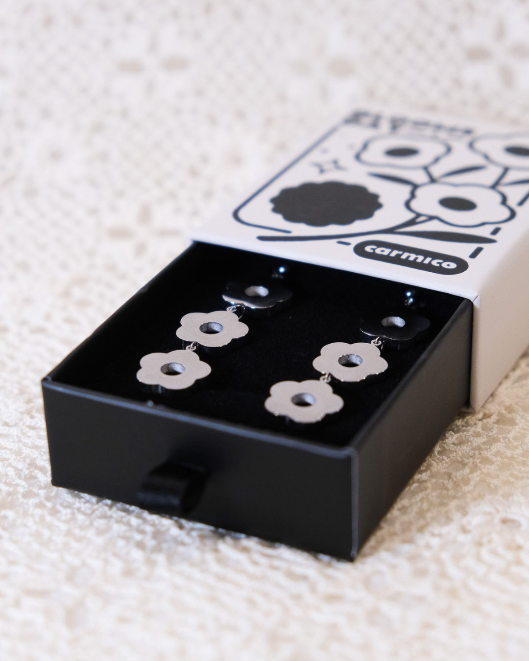 Silver daisy dangle earrings in their packaging.