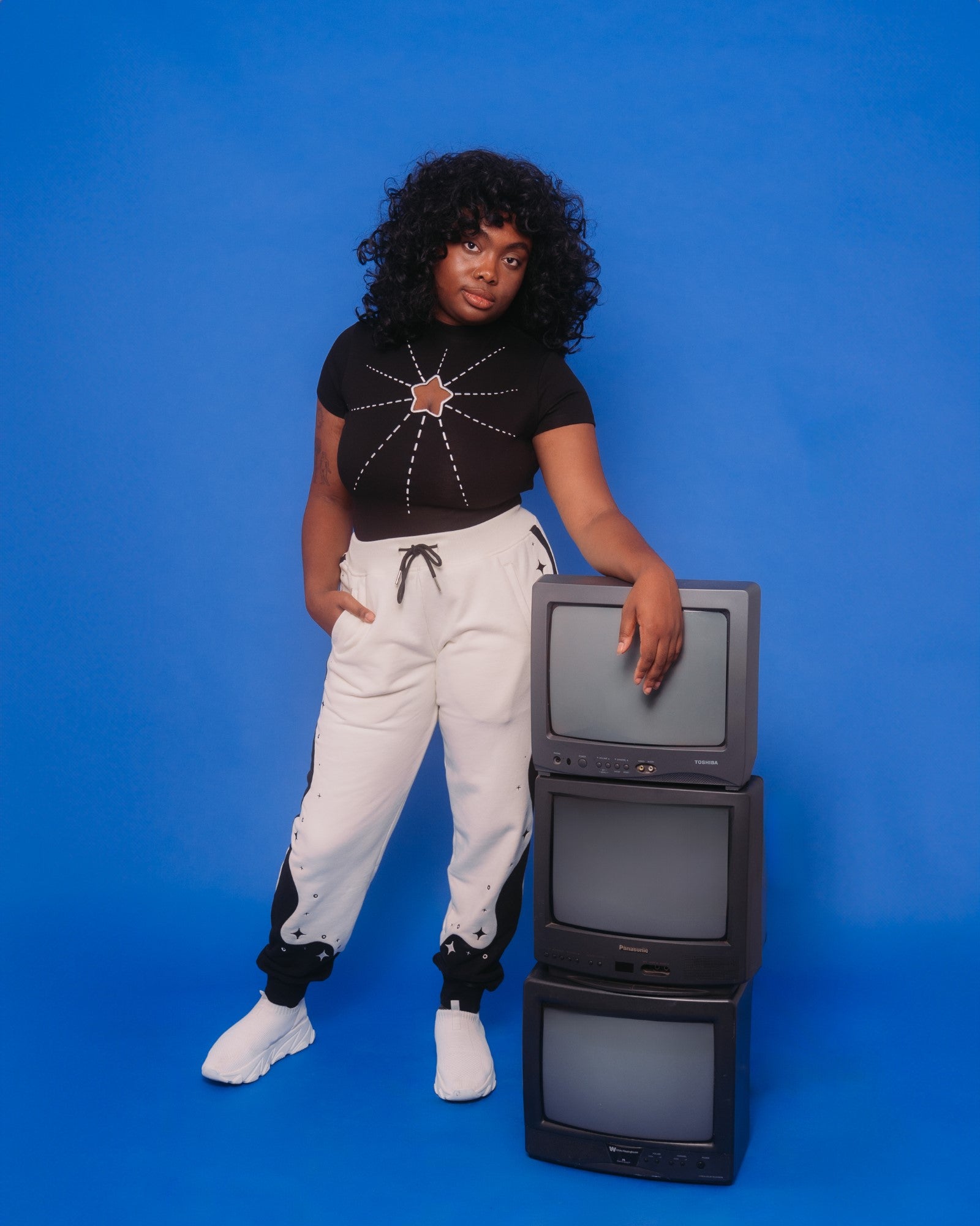 Woman wearing supernova joggers in size large posing with three stacked tvs.